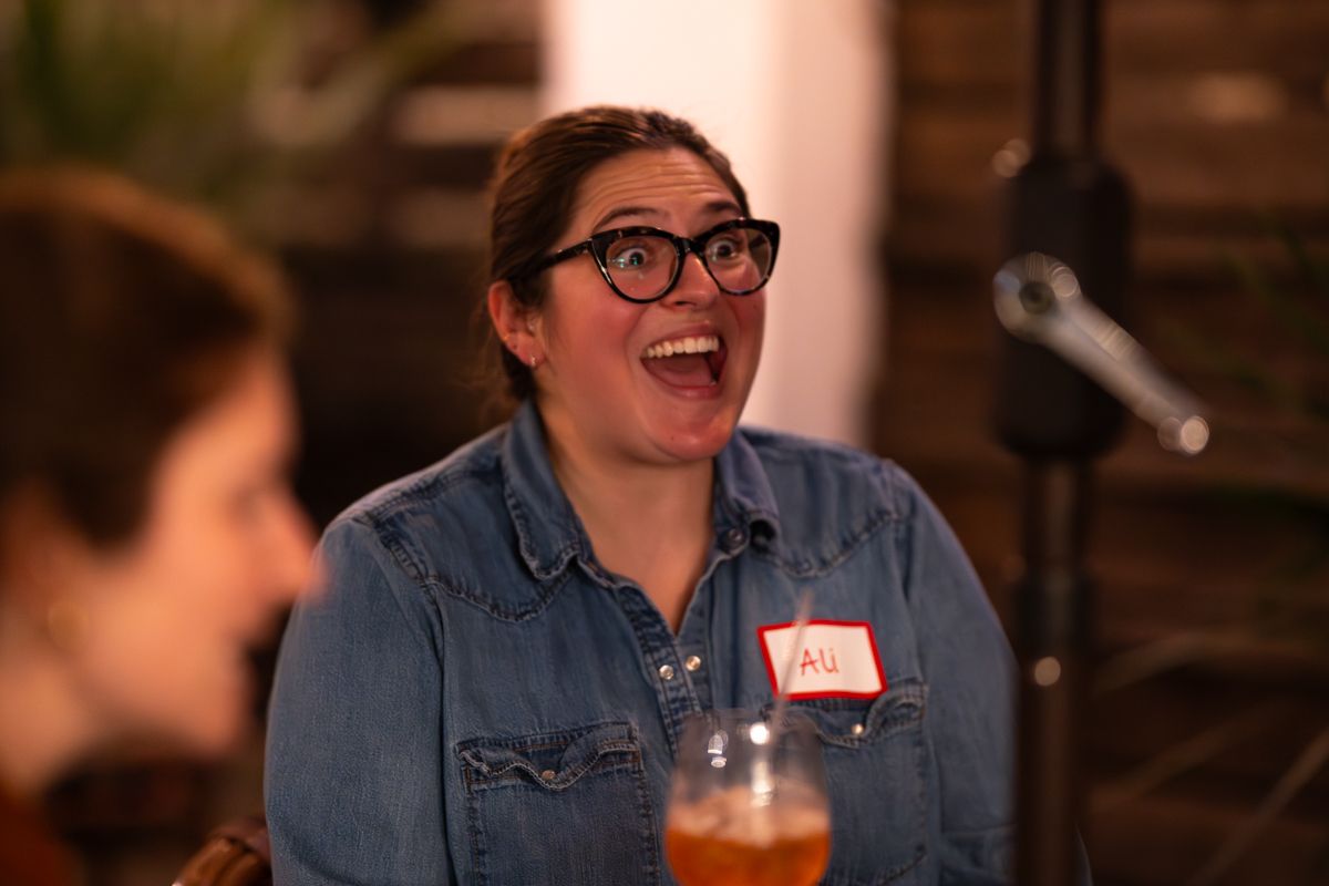 A person in a denim jacket and glasses sits in a dimly lit restaurant setting.