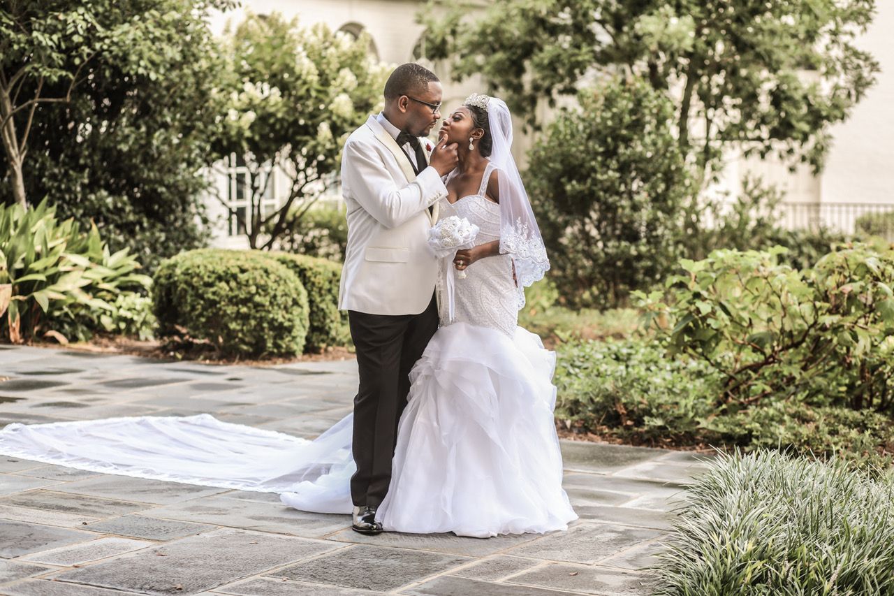 Wedding couple shares romantic moments in a lush garden setting with white dress and formal attire.