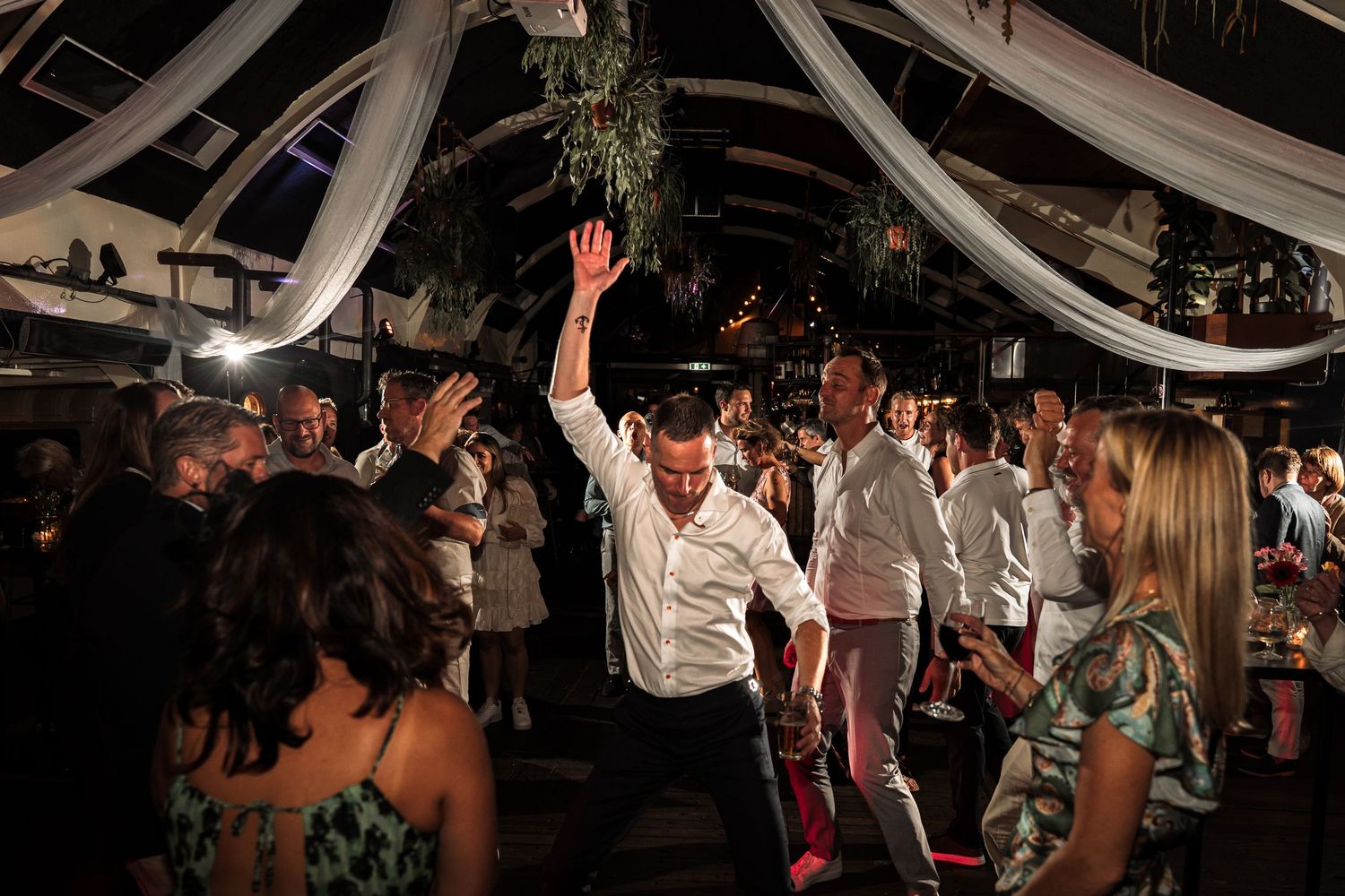 Wedding guests dance and celebrate on a crowded dance floor under a white tent during an evening reception.