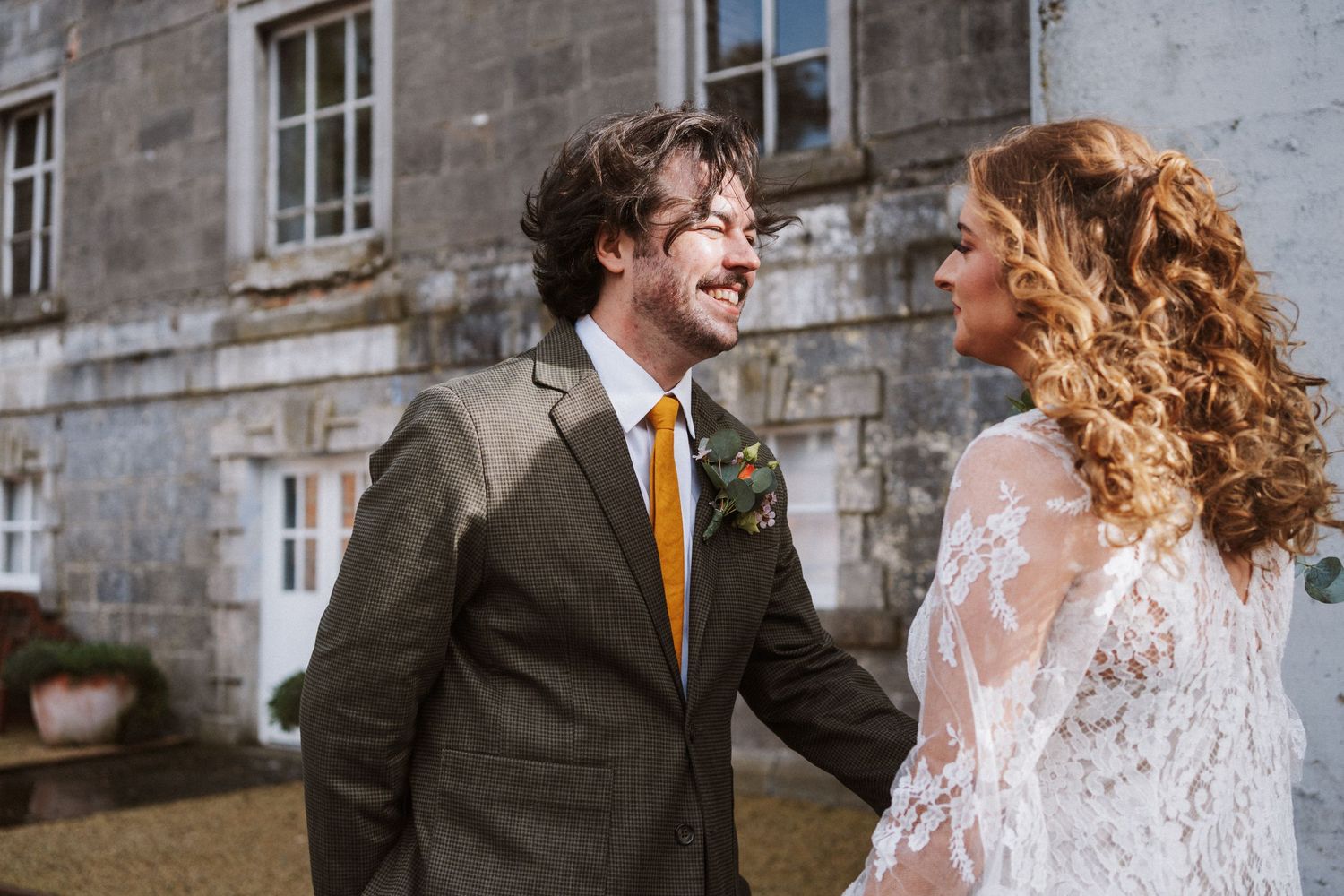 A couple shares joyful moments in front of a historic stone building wearing wedding attire.
