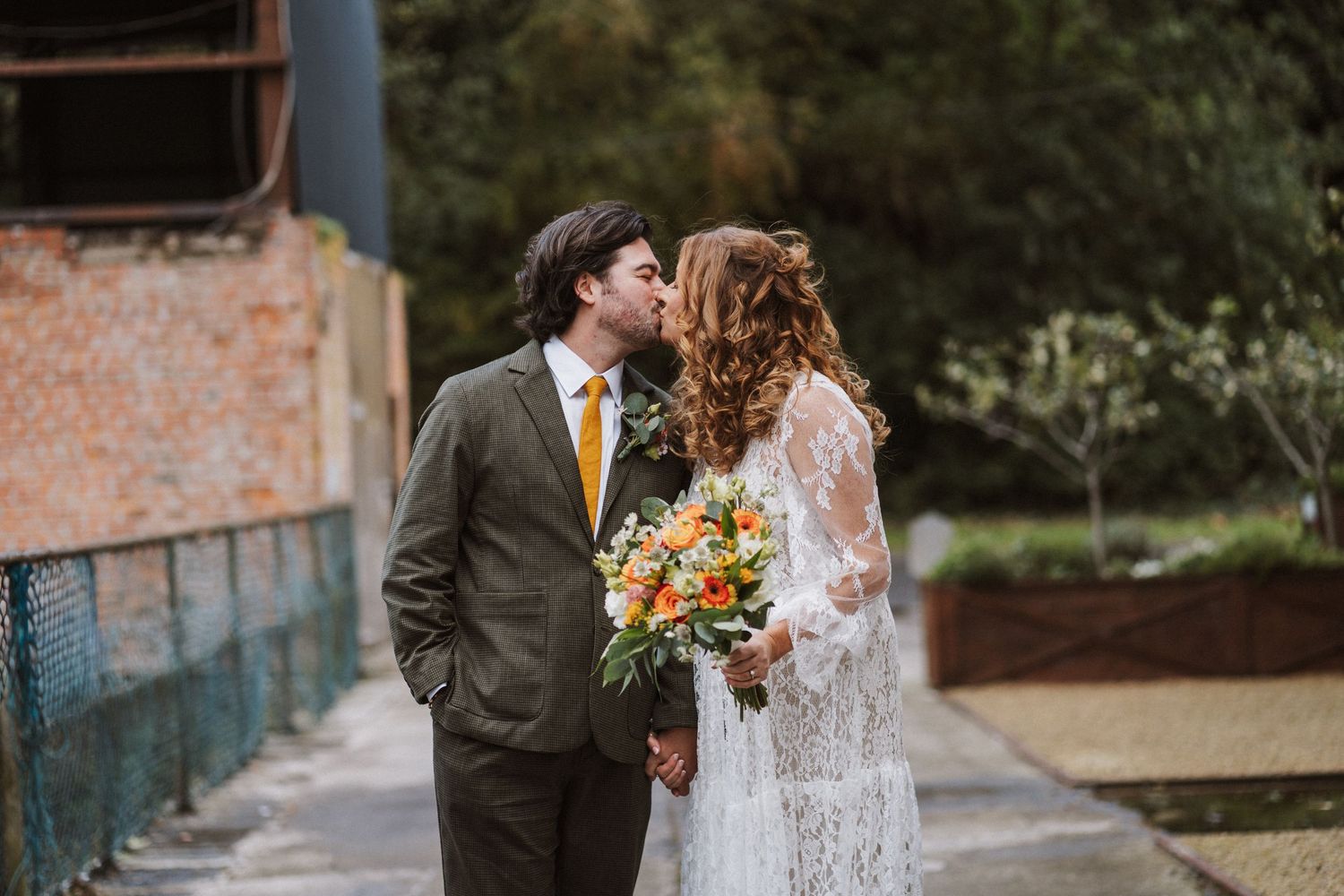 Romantic wedding couple shares intimate moments in an outdoor garden setting with rustic brick walls and natural greenery.