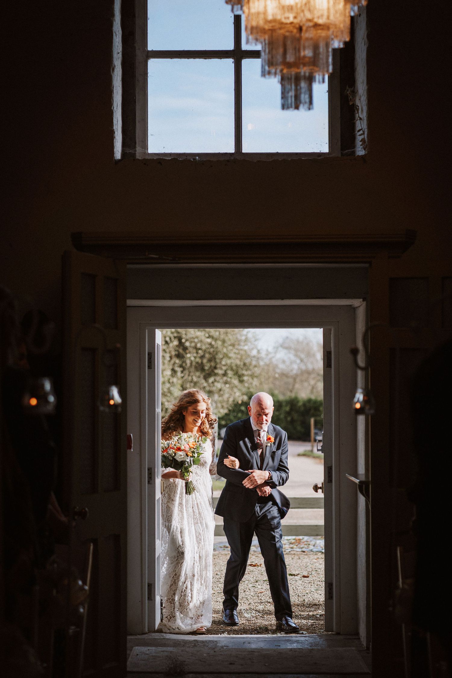 Silhouettes of people framed in a doorway against bright outdoor light creating a dramatic wedding scene.