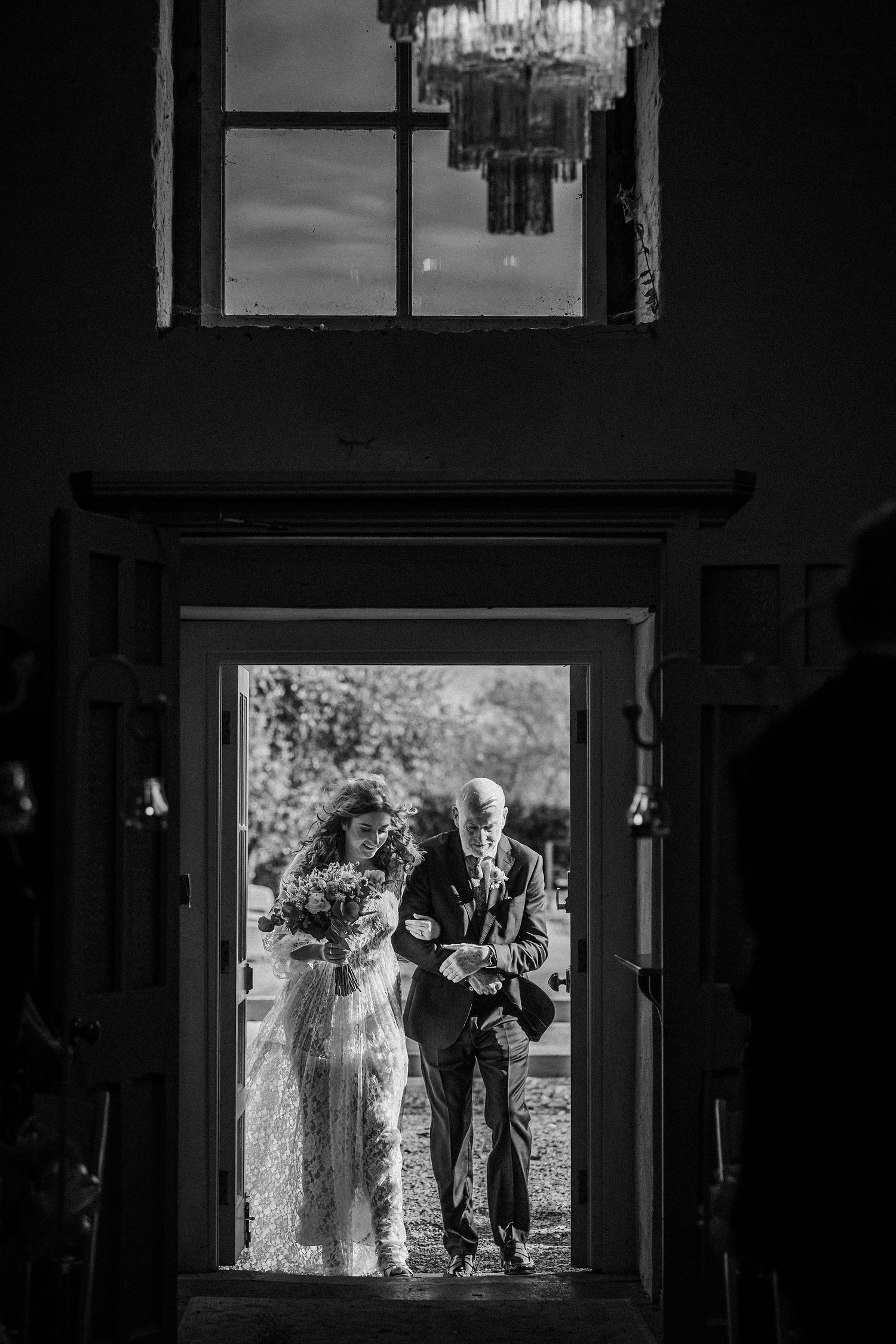 A black and white silhouette of people standing in a doorway framed by window light during a wedding ceremony.