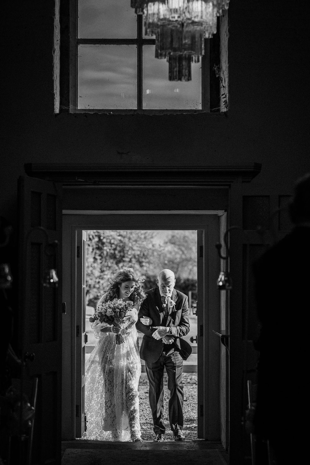 A black and white silhouette of people standing in a doorway framed by window light during a wedding ceremony.