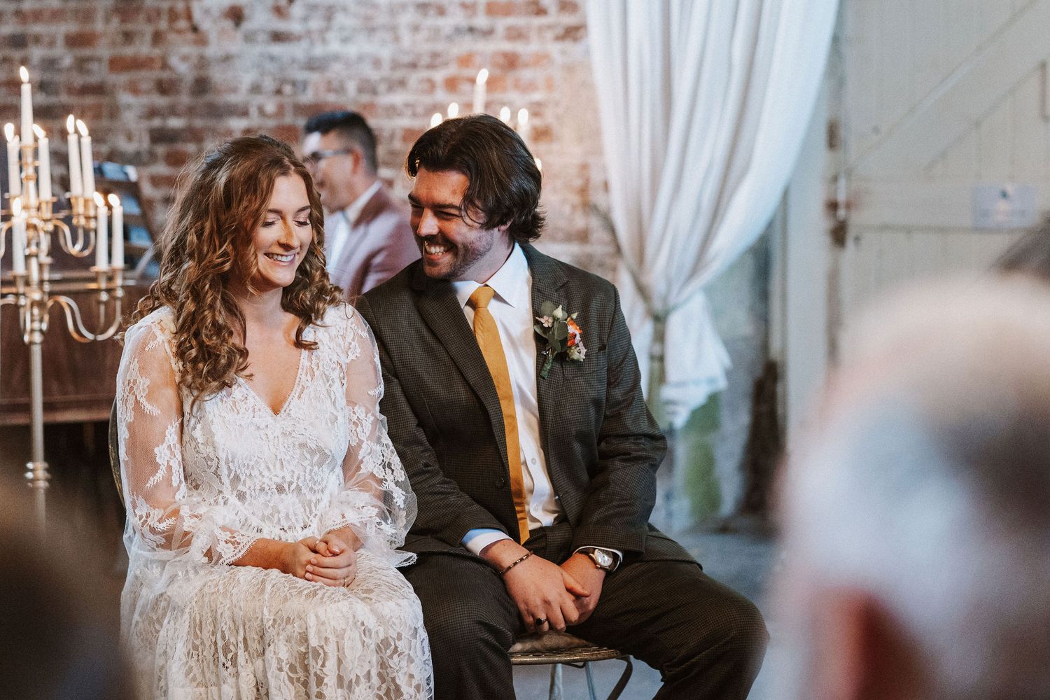A couple shares a joyful moment together during their wedding ceremony in a rustic brick-walled venue.