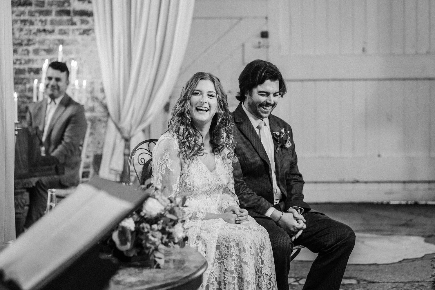 A happy couple sits together during their wedding ceremony in a black and white photograph.