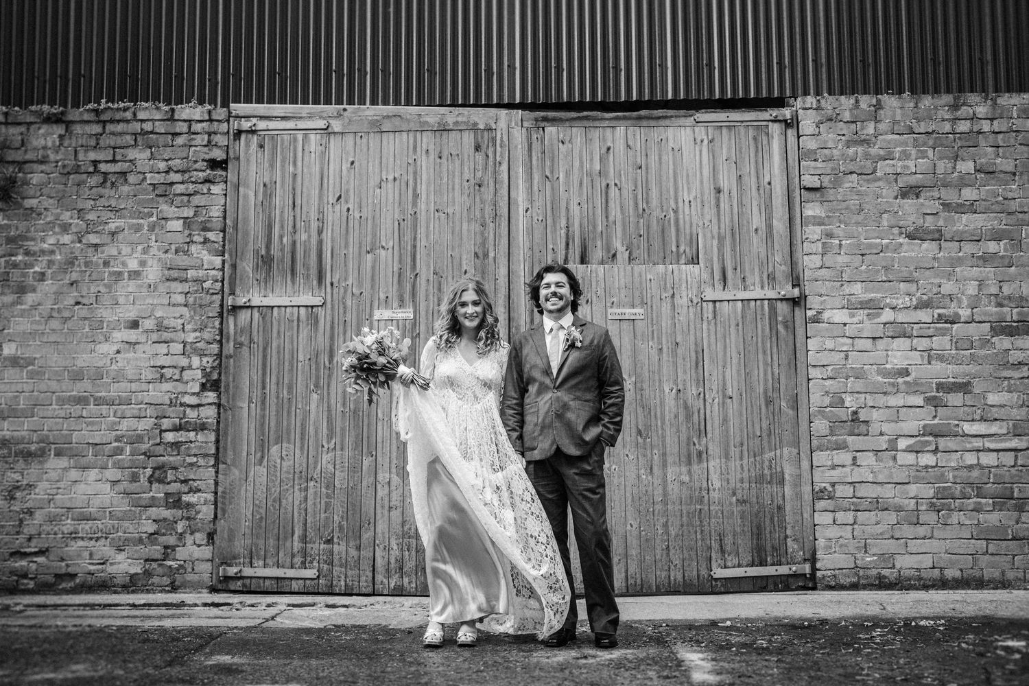 A black and white panoramic sequence showing a couple posing against rustic wooden barn doors.