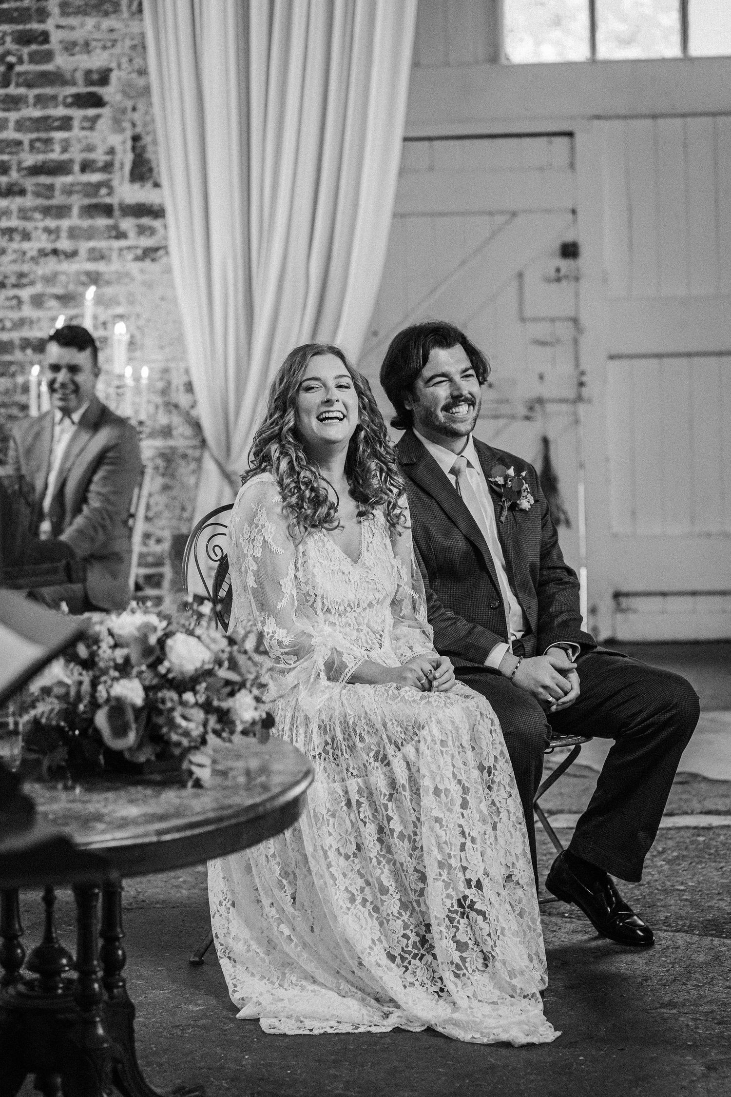 A joyful wedding moment captured in black and white showing a couple sharing genuine laughter during their celebration.
