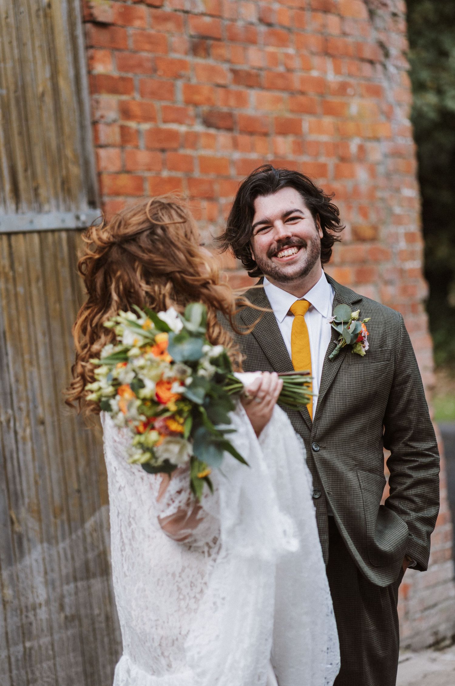 Candid wedding photo sequence showing playful moments between newlyweds with orange bouquet against brick wall.
