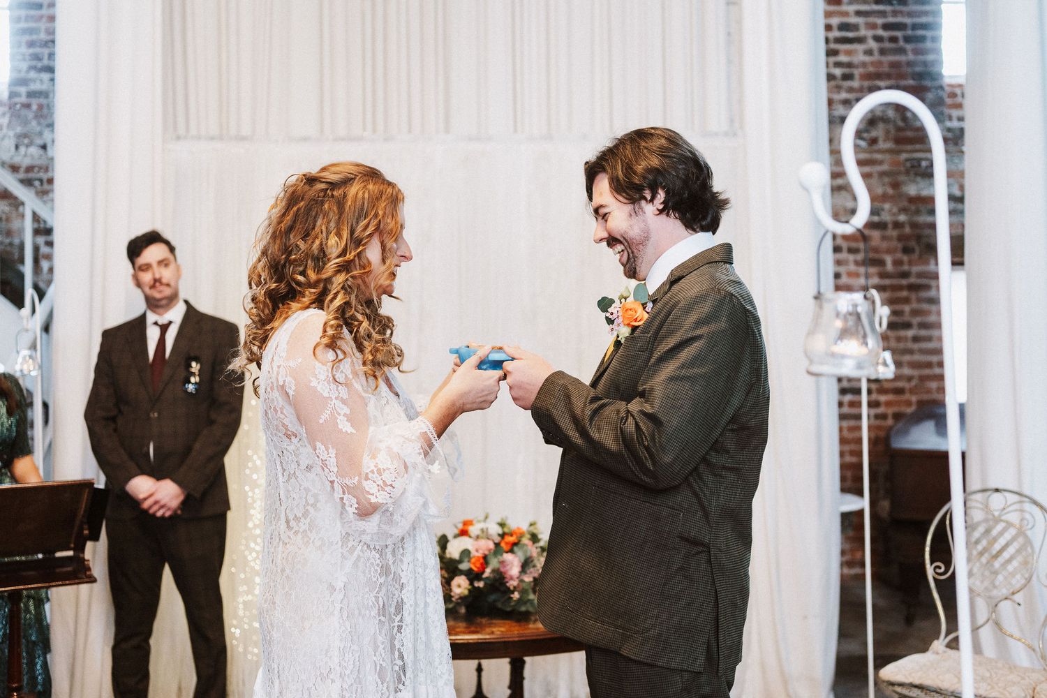 A couple exchanges rings during their wedding ceremony in front of a white-columned brick church interior.