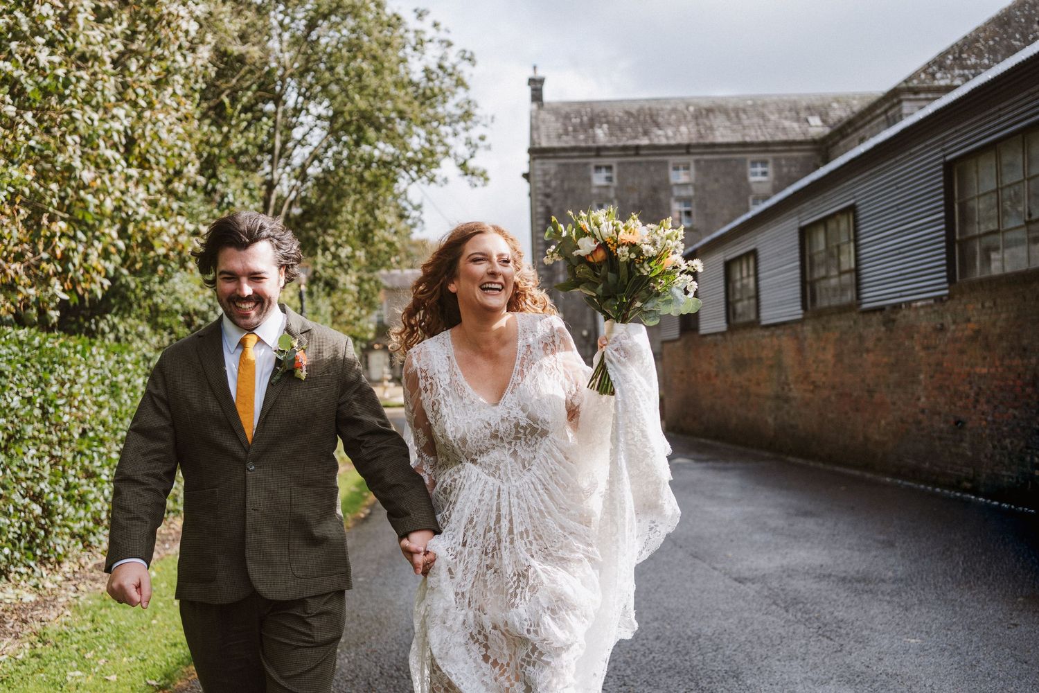 A couple shares a joyful moment walking together in formal attire along a stone pathway.