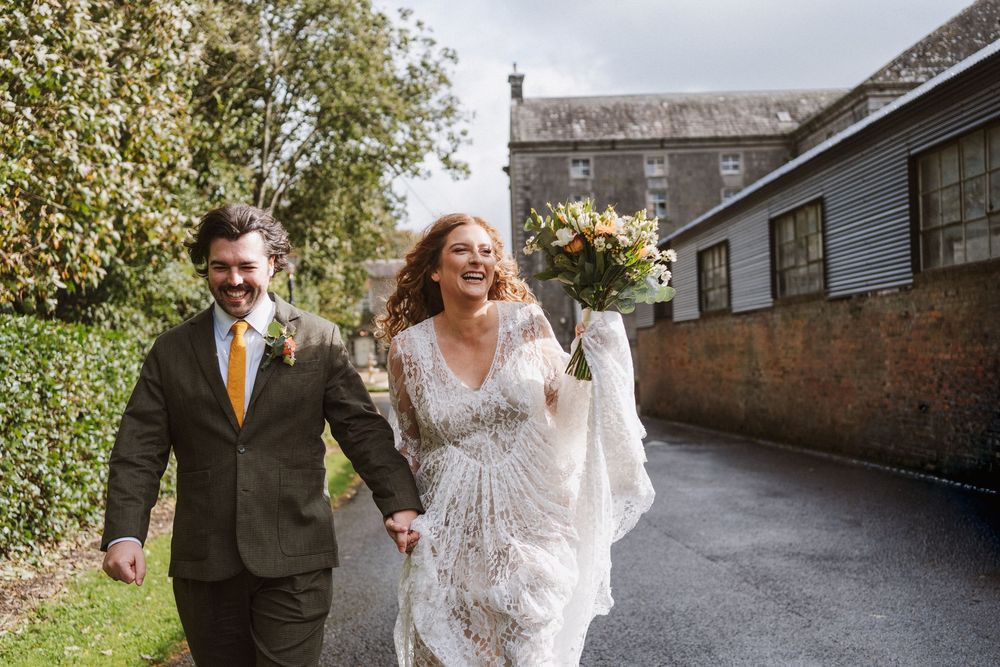 A couple shares a joyful moment walking together in formal attire along a stone pathway.