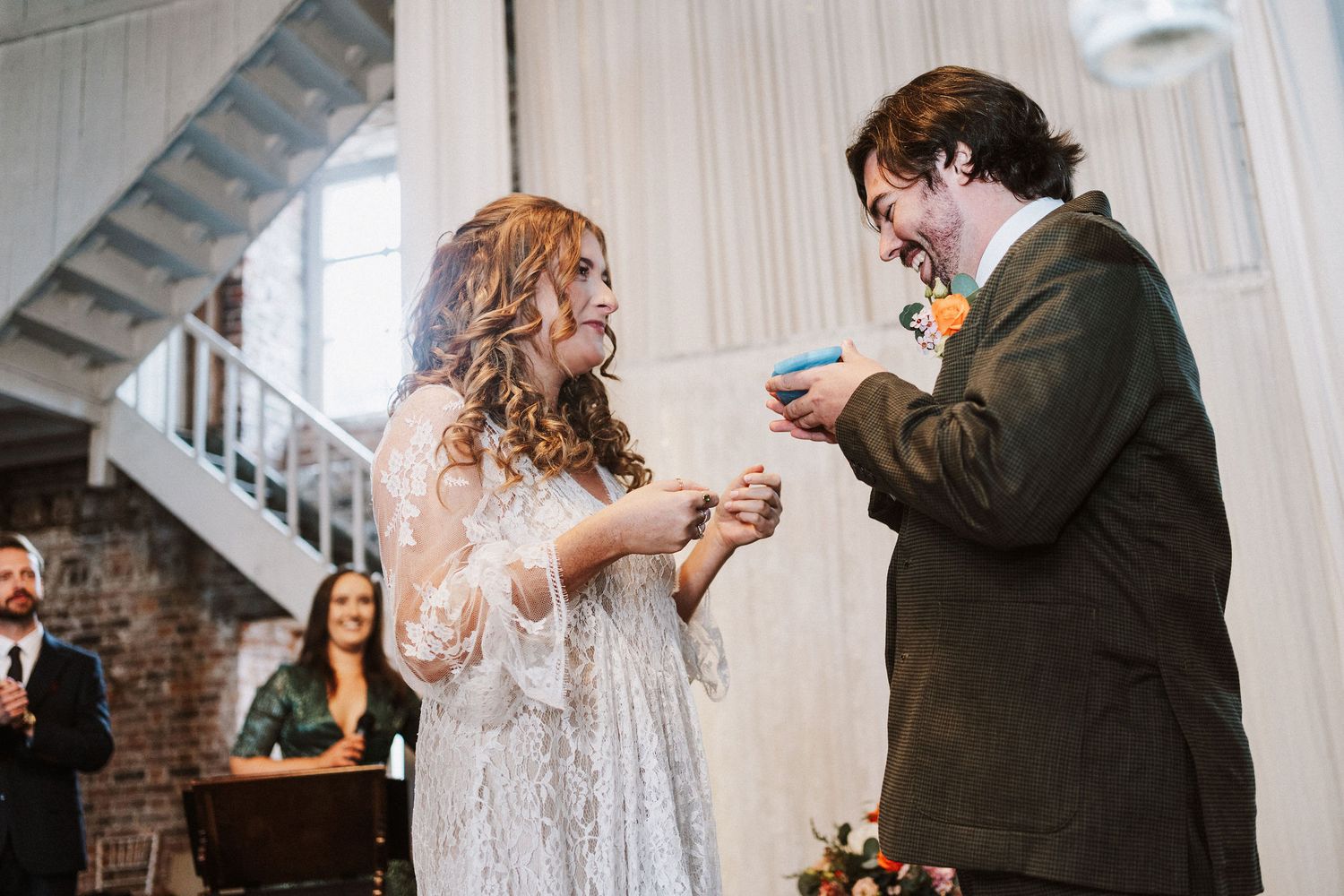 A couple exchanges rings during an intimate indoor wedding ceremony in a rustic brick-walled venue.