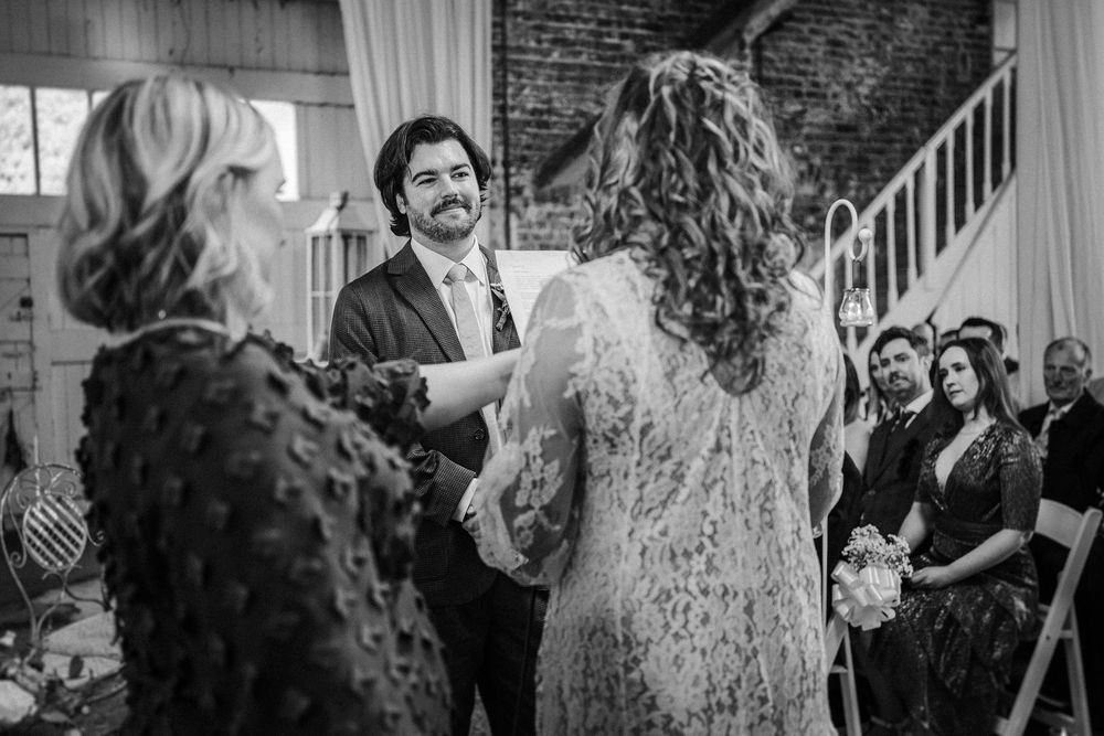 A black and white photo captures a joyful moment during a wedding ceremony in an industrial-style venue.