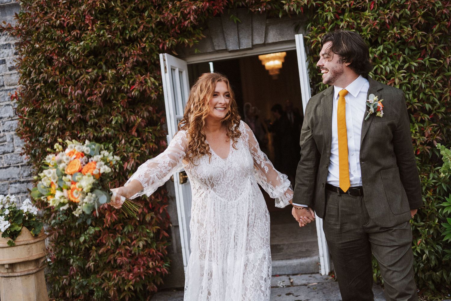 Bride and groom share a joyful moment outdoors with autumn foliage in the background.