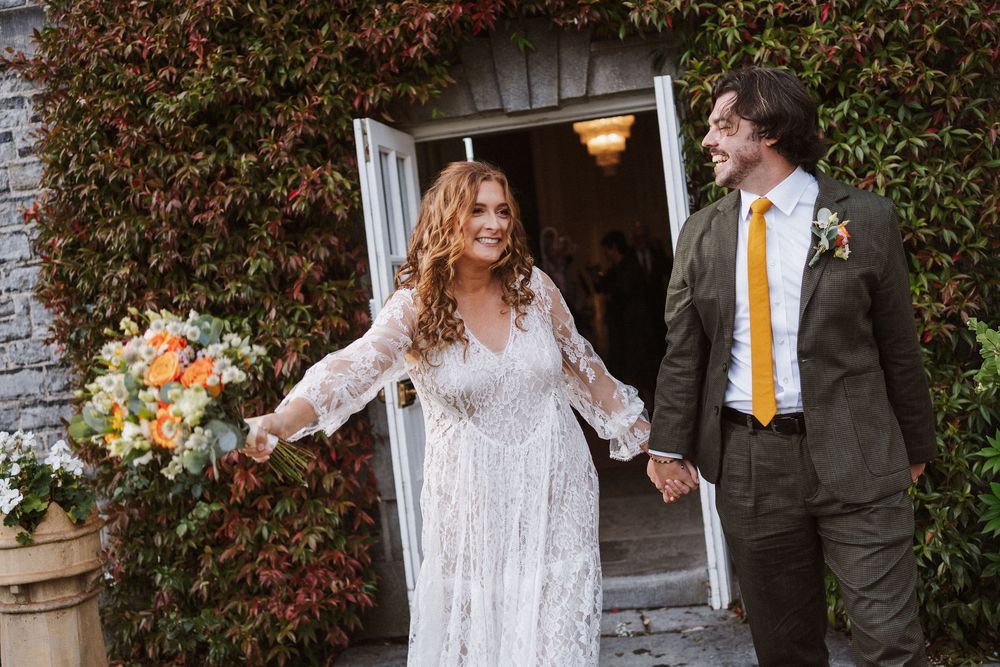 Bride and groom share a joyful moment outdoors with autumn foliage in the background.