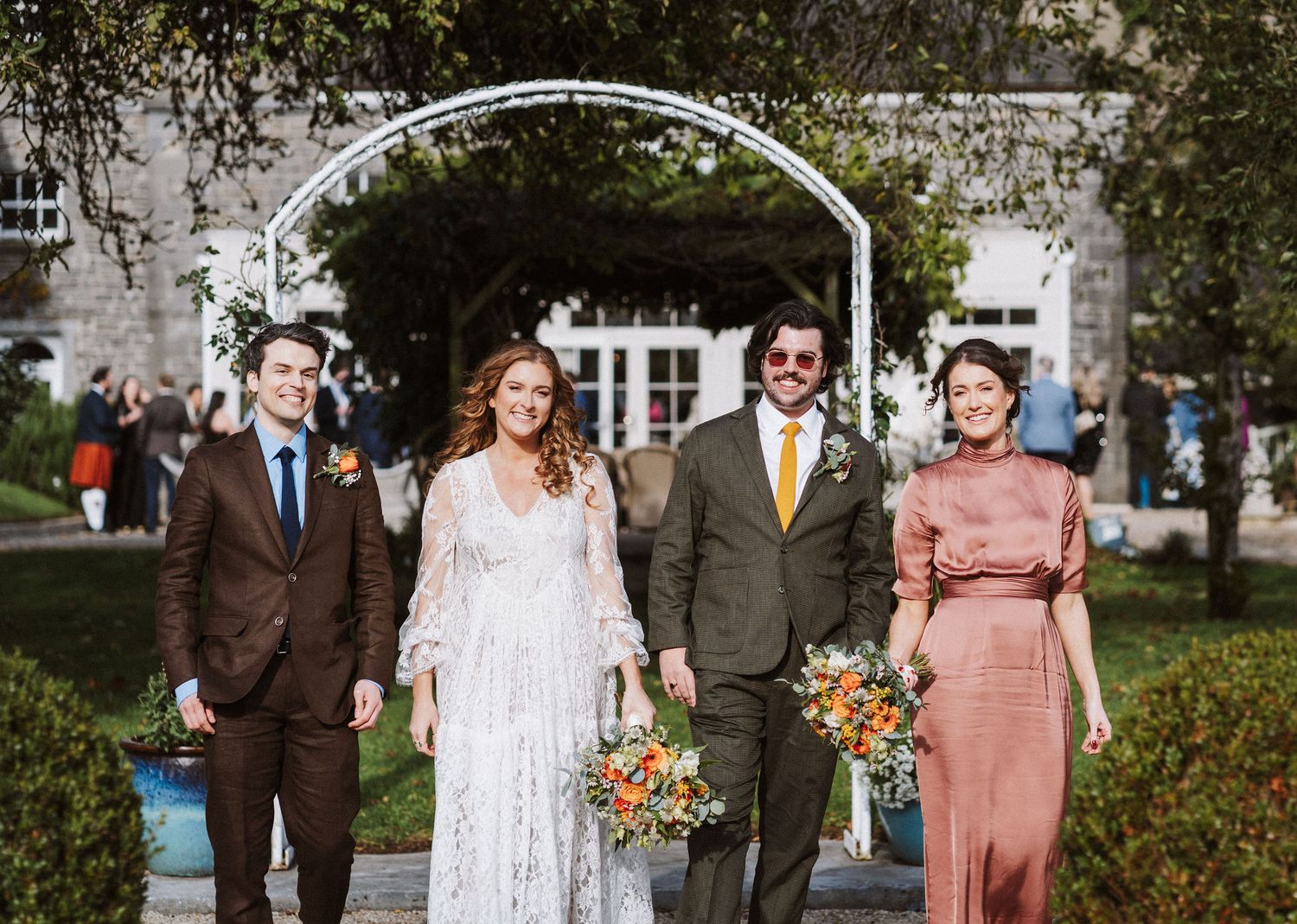 Wedding party members pose outdoors in coordinated brown and peach attire on a sunny autumn day.
