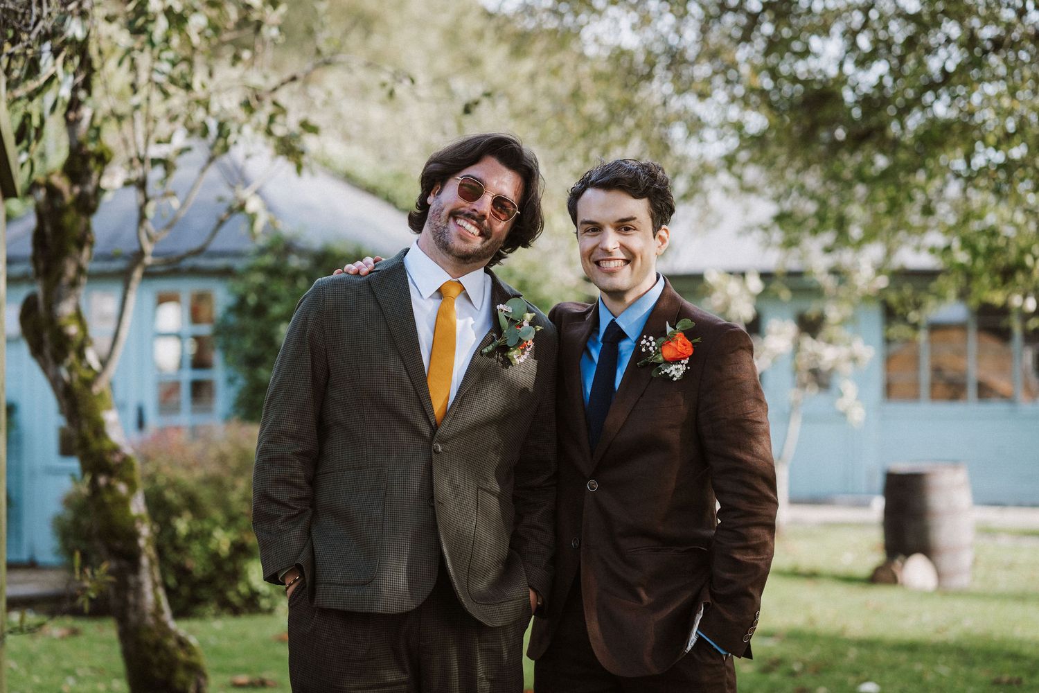 Wedding party smiles and laughs together while standing on grass under trees in autumn.
