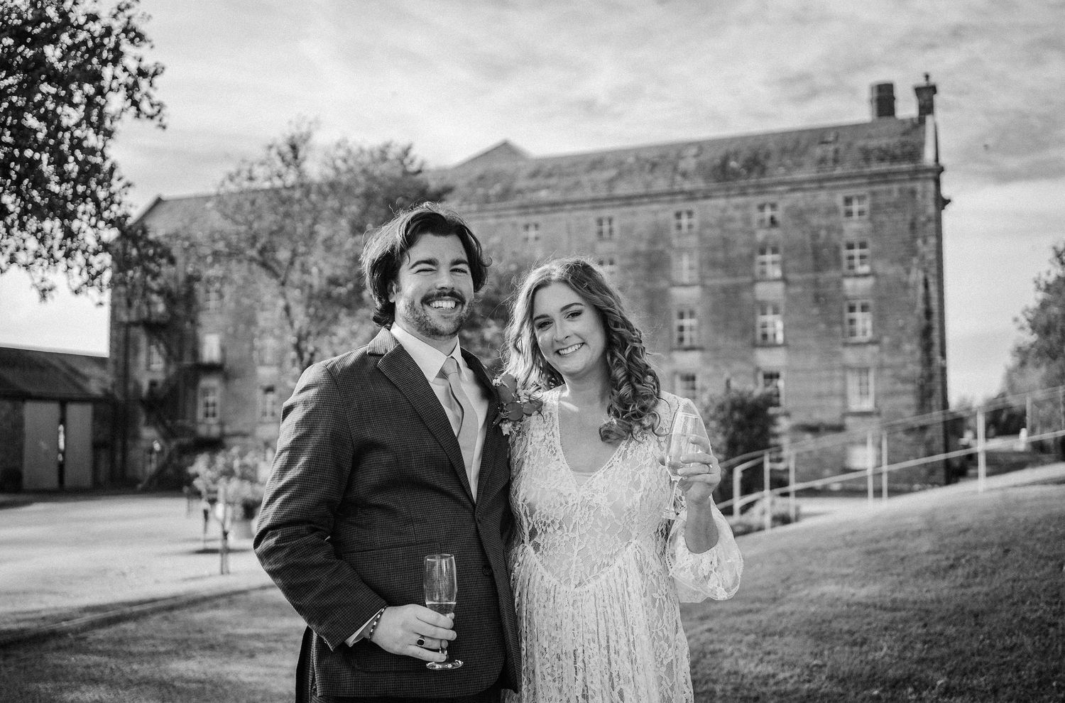 A couple shares a romantic moment on the grounds of a historic stone building during their wedding celebration.