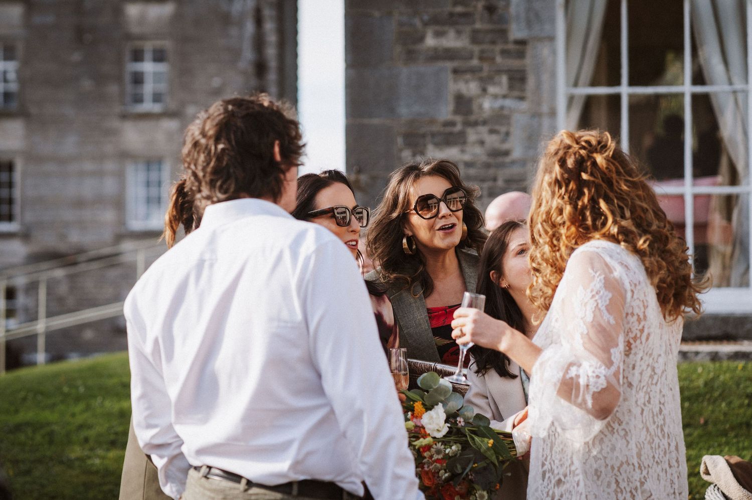 Wedding party members laugh and celebrate together during an outdoor summer reception.