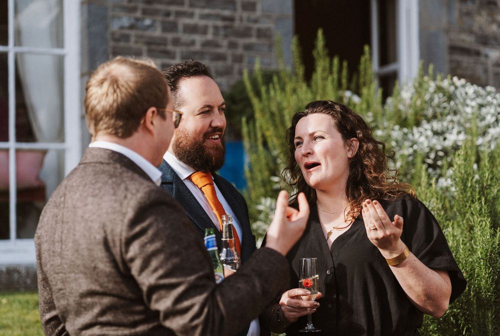 A group of people in formal attire socialize and laugh together at an outdoor garden party.