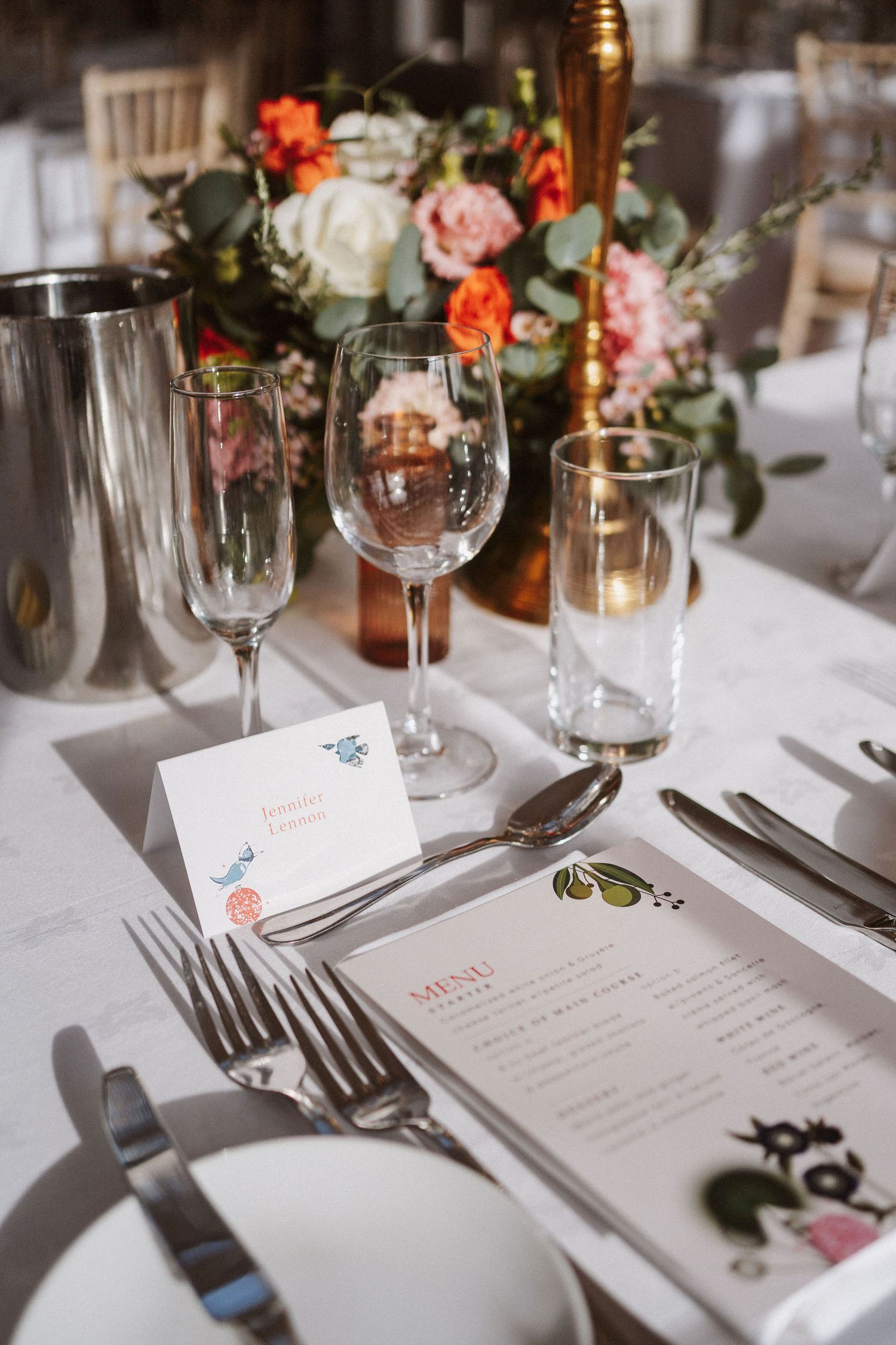 Elegant wedding reception table setting with white linens, floral centerpieces, menu cards and crystal glassware.