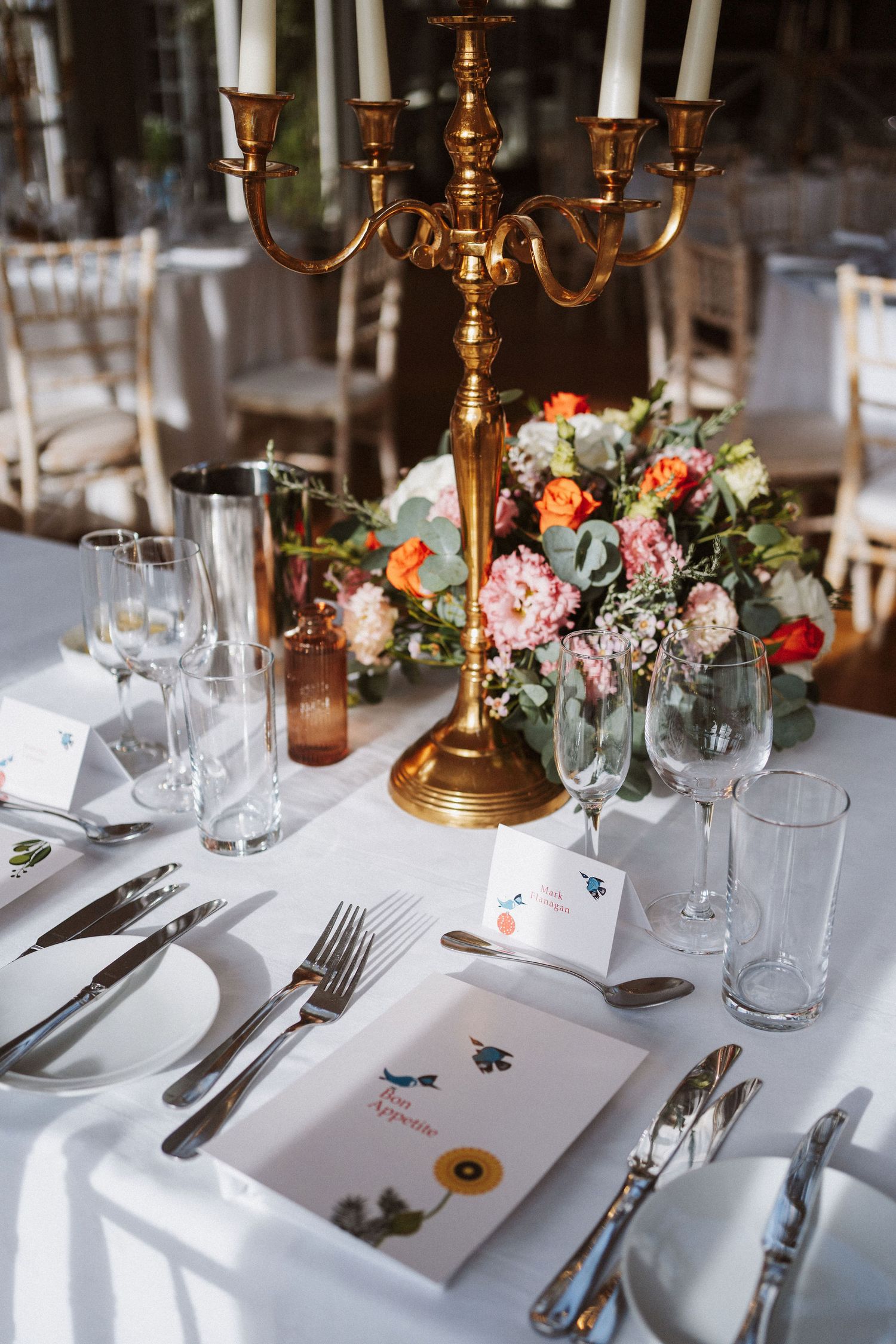 Elegant wedding table settings with gold candelabras, pink floral arrangements, and white linens at a formal reception.