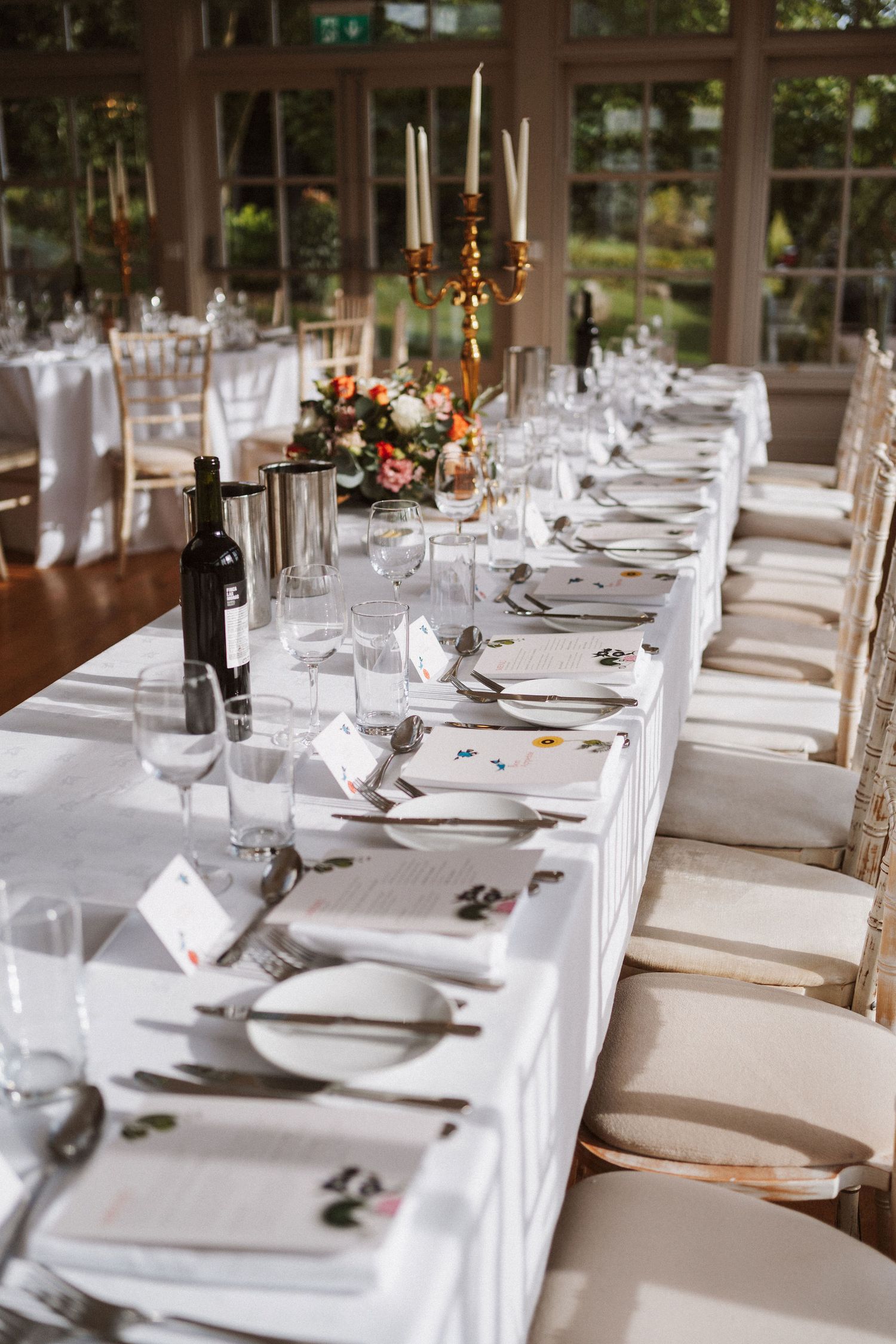 Elegant wedding reception tables set with white linens, wine glasses, and place settings in a bright sunlit venue.