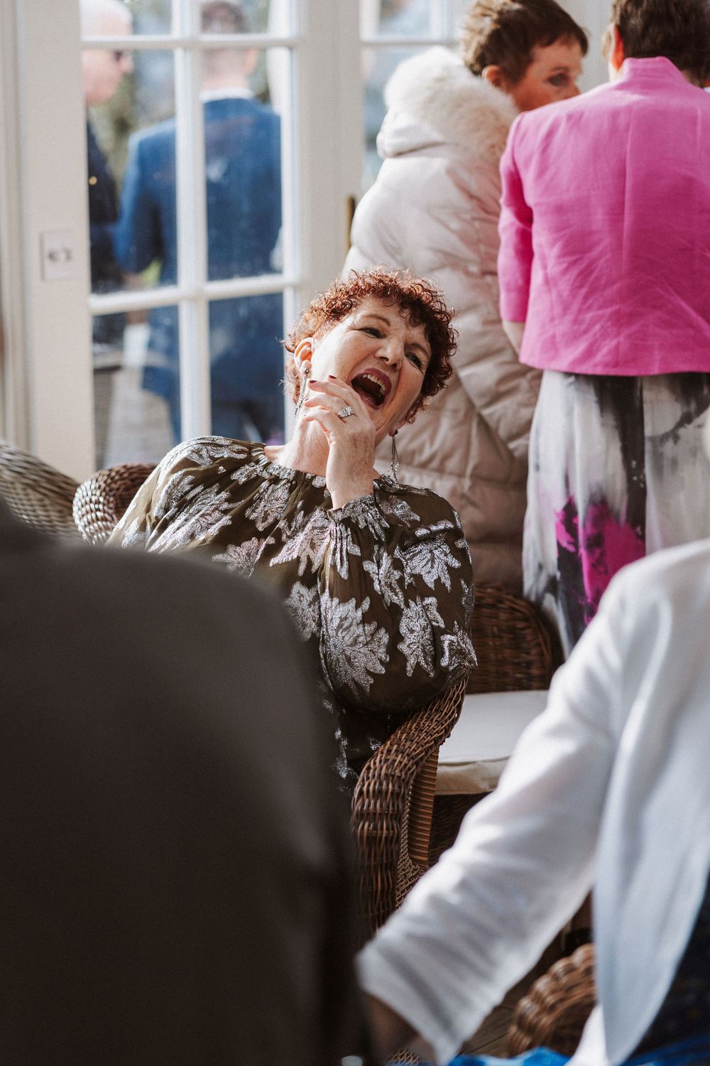 A person in a chair laughs joyfully while being attended to by caregivers in white and pink uniforms.