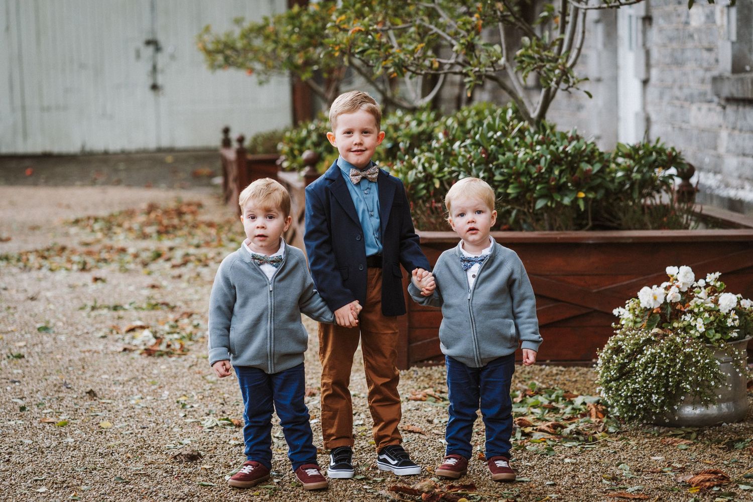 Three young children play and laugh together in a garden setting with raised wooden planter boxes.
