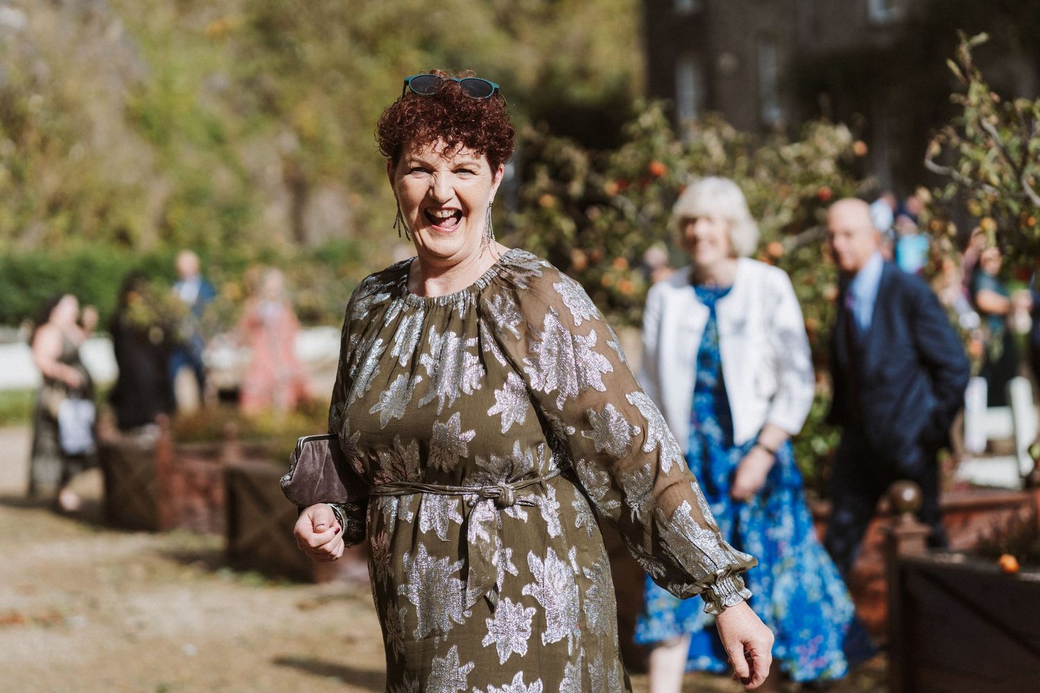 A joyful outdoor wedding celebration with guests gathered in a natural setting surrounded by trees and sunlight.