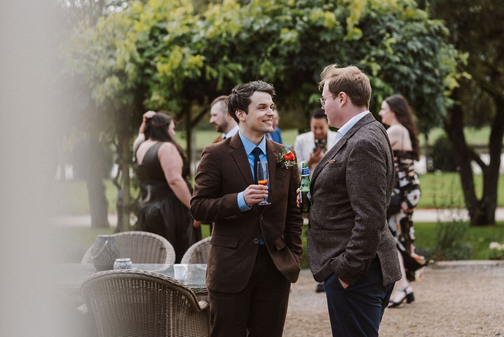 Wedding party members in formal attire share laughs and drinks during an outdoor celebration.