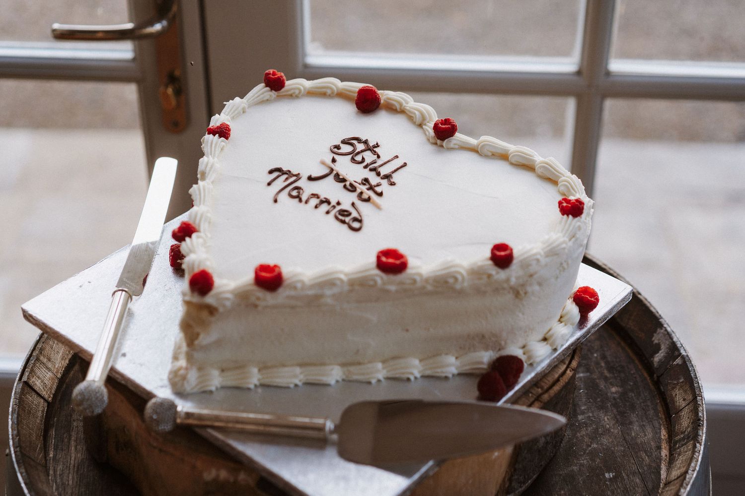 A white frosted cake decorated with red cranberries and pine sprigs sits on a rustic wooden table.
