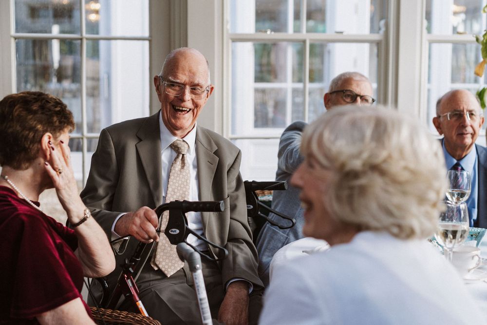 Group of senior citizens enjoying conversation and laughter during a social gathering at a bright indoor venue.