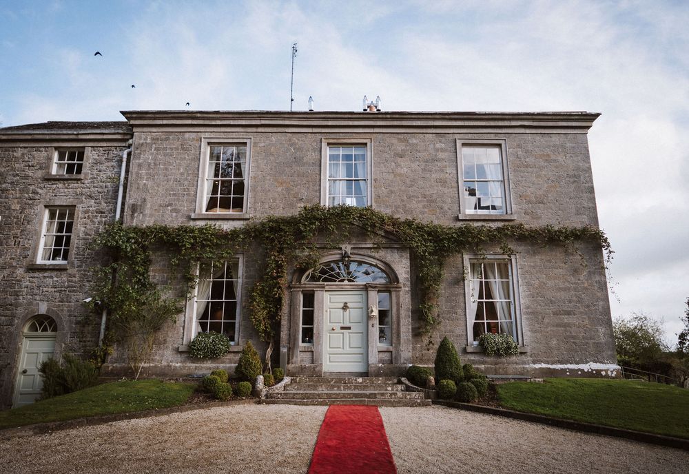 A panoramic view of a historic stone manor house with a red carpet entrance leading to its elegant facade.