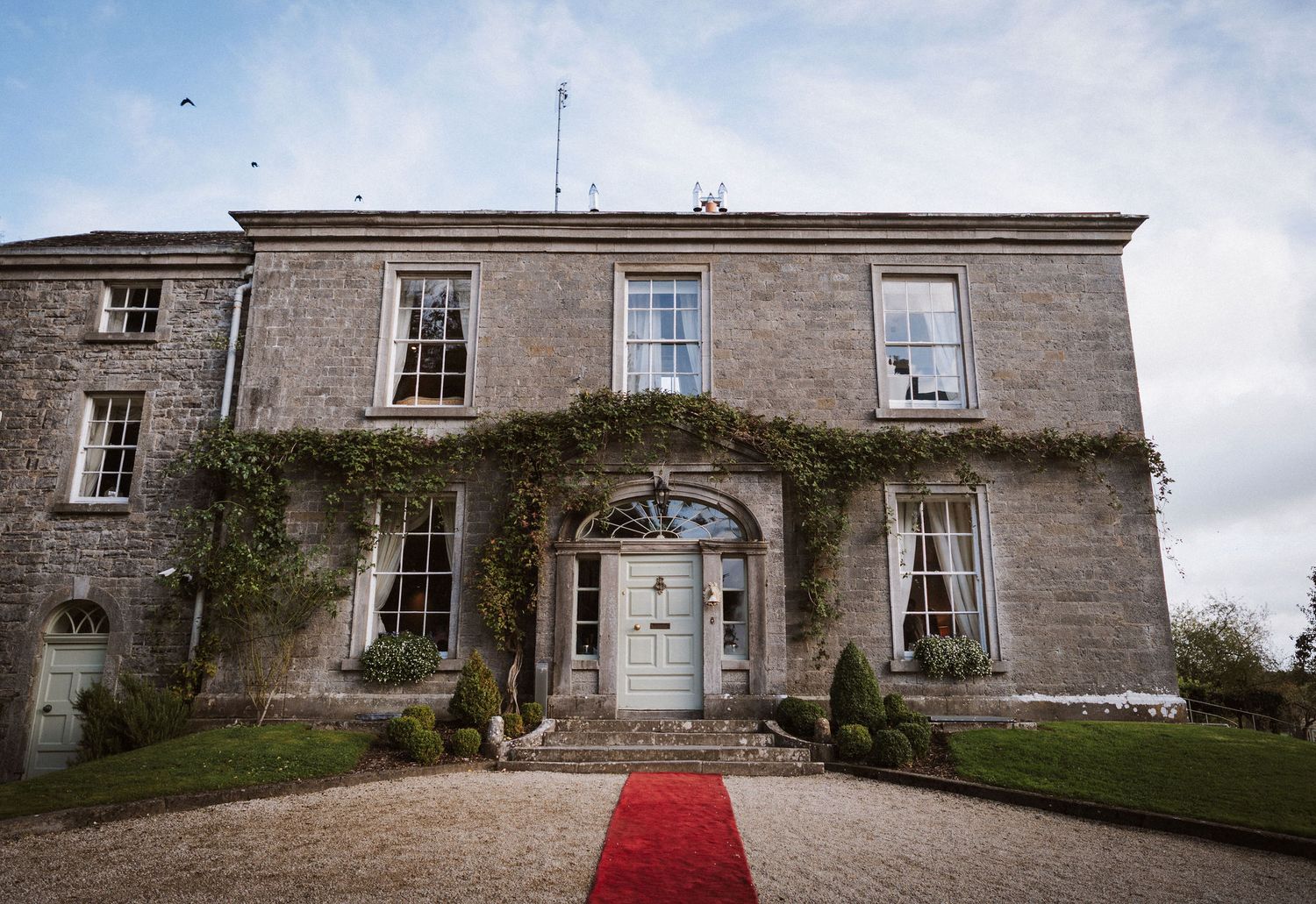 A panoramic view of a historic stone manor house with a red carpet entrance leading to its elegant facade.