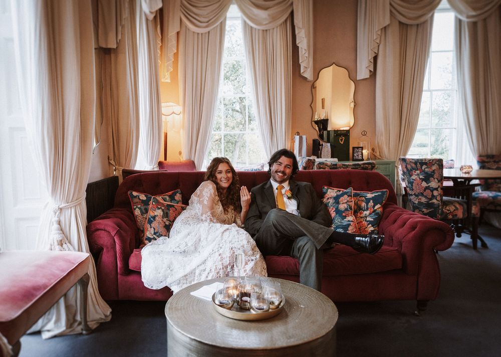 Elegant reception room with red velvet sofas, cream drapes, and ornate decor during a wedding celebration.