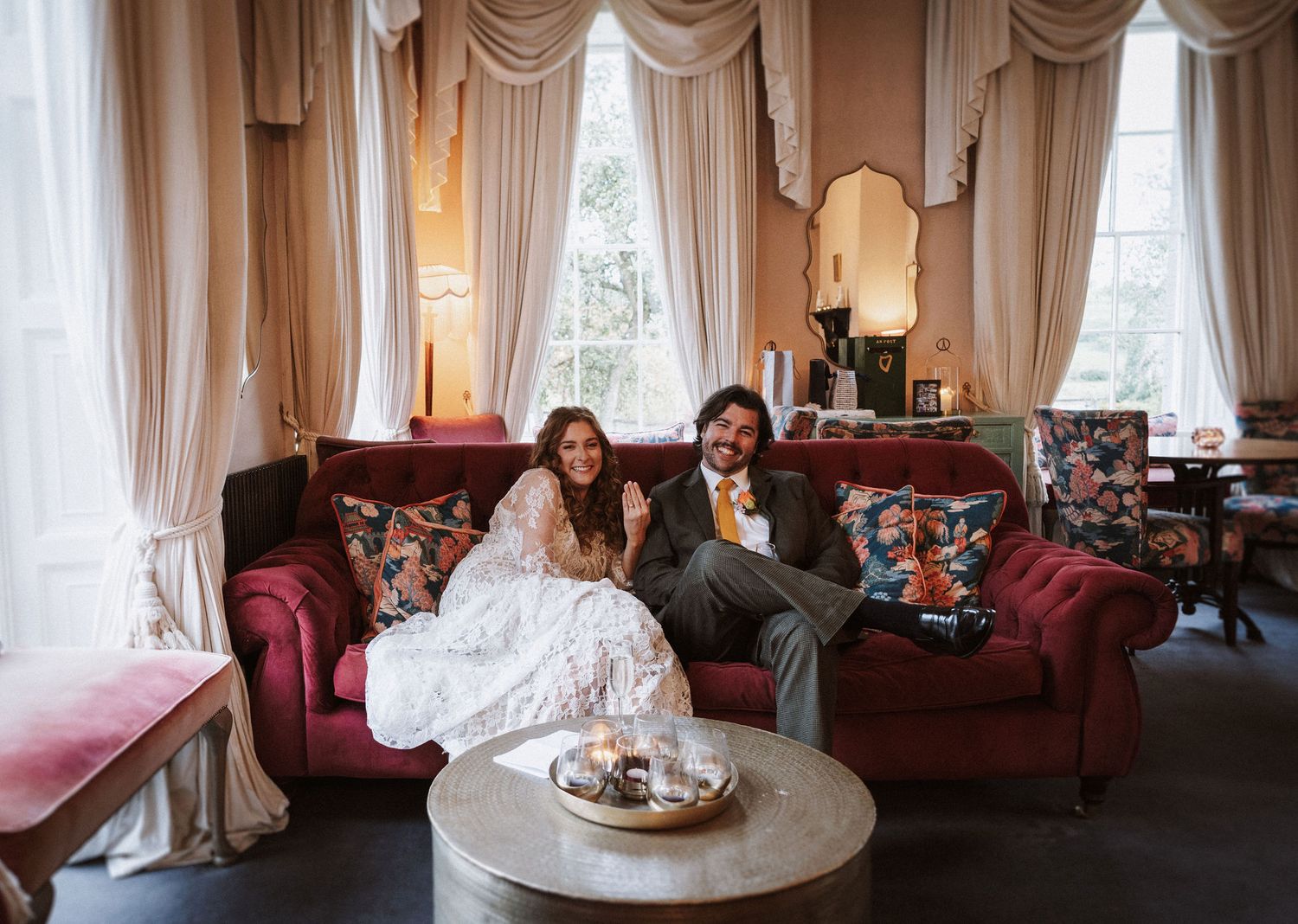 Elegant reception room with red velvet sofas, cream drapes, and ornate decor during a wedding celebration.