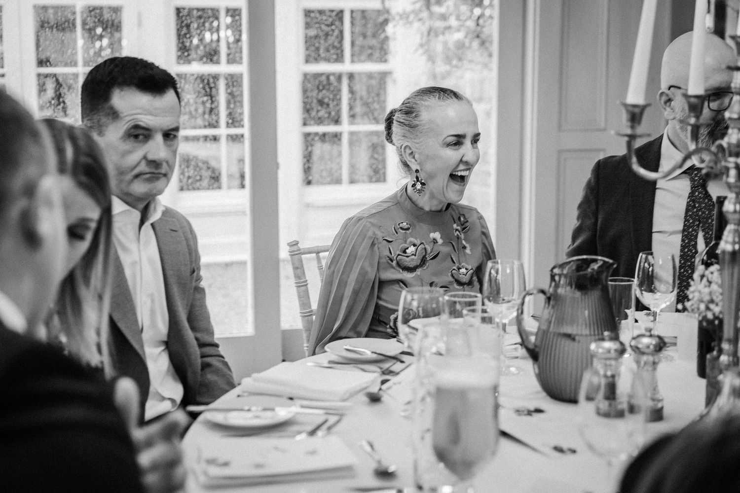 Black and white photo of guests seated at a formal dinner table with glassware and place settings.