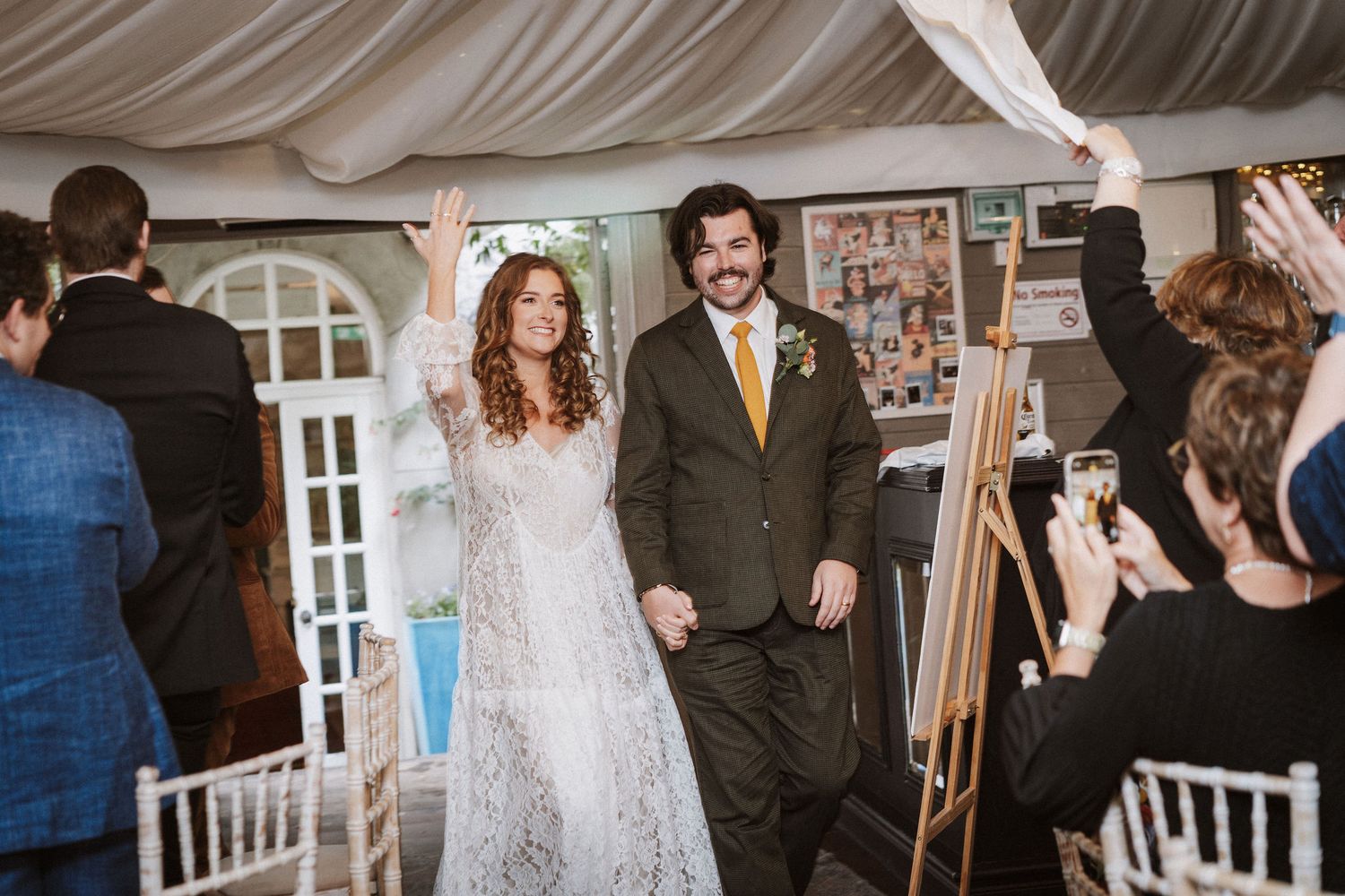 Wedding guests mingling in a bright indoor venue with white chairs and elegant decor.