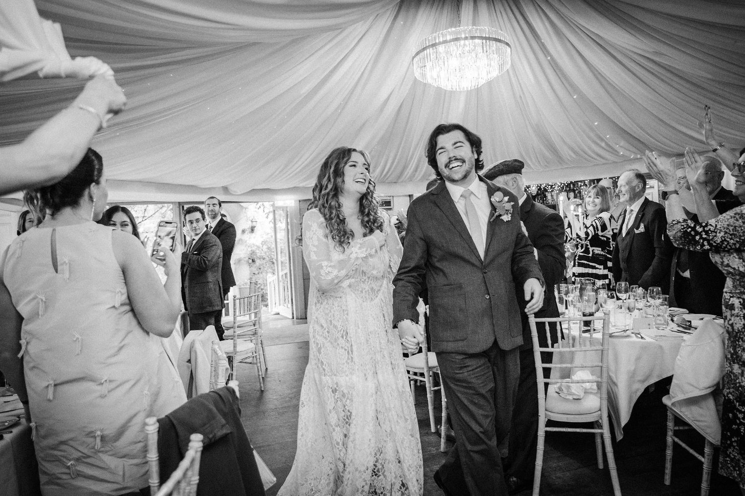 Wedding guests dance and celebrate under an elegant white tent during a joyful reception celebration.
