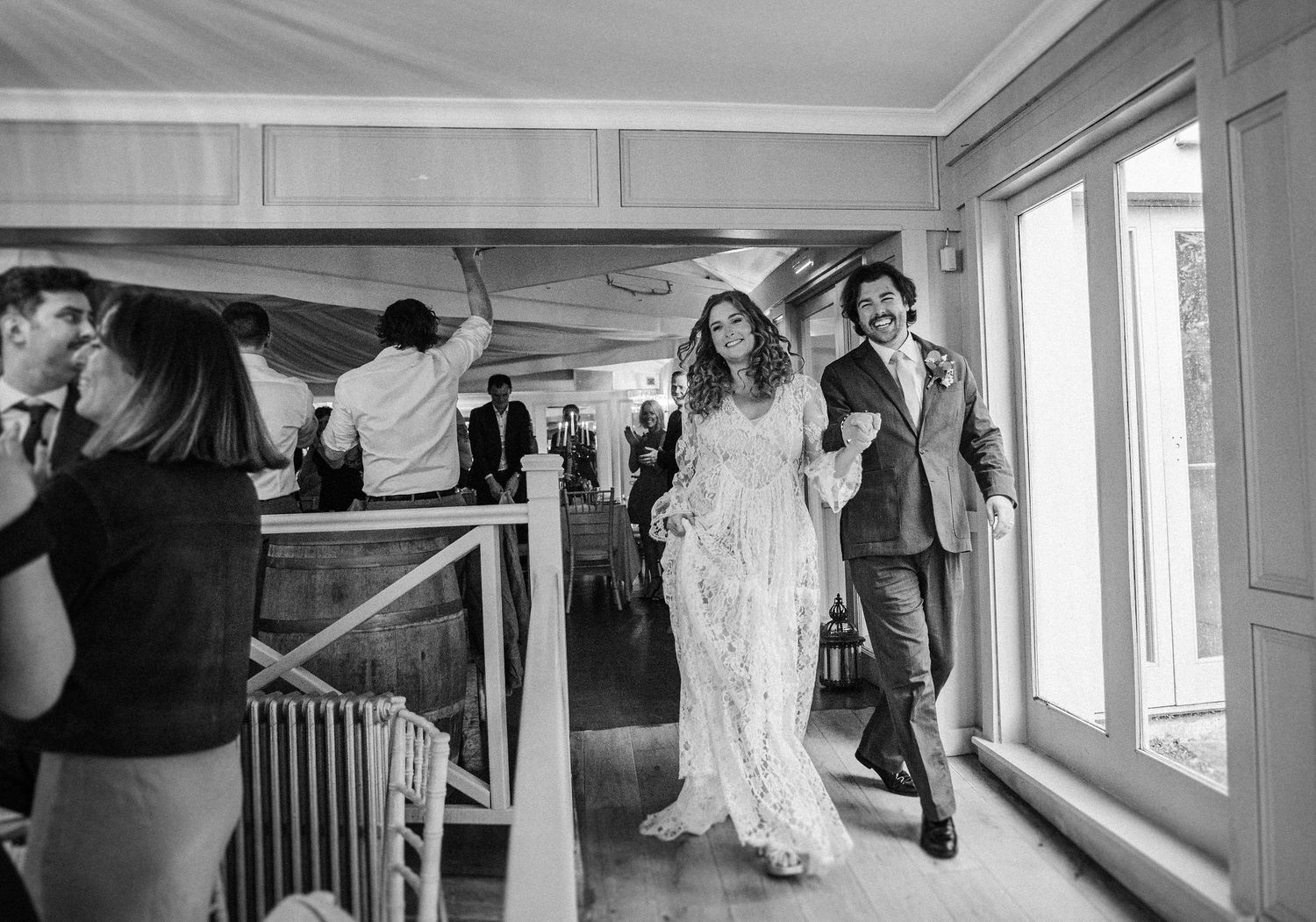 Black and white panoramic wedding photo sequence showing candid moments of preparation and celebration in a bright room.