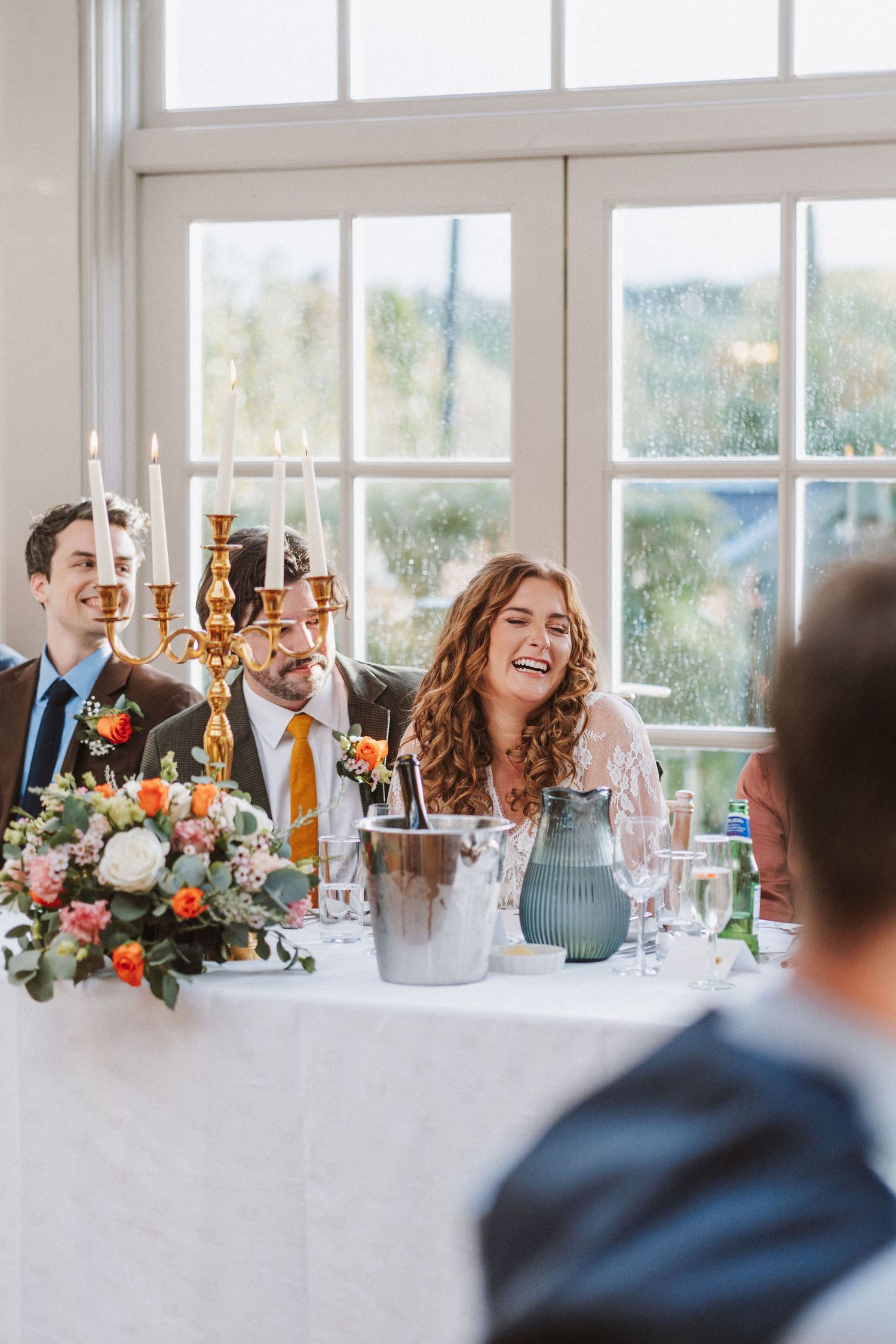 Wedding reception guests enjoying dinner and conversation at elegant table with floral centerpieces and candlelight.