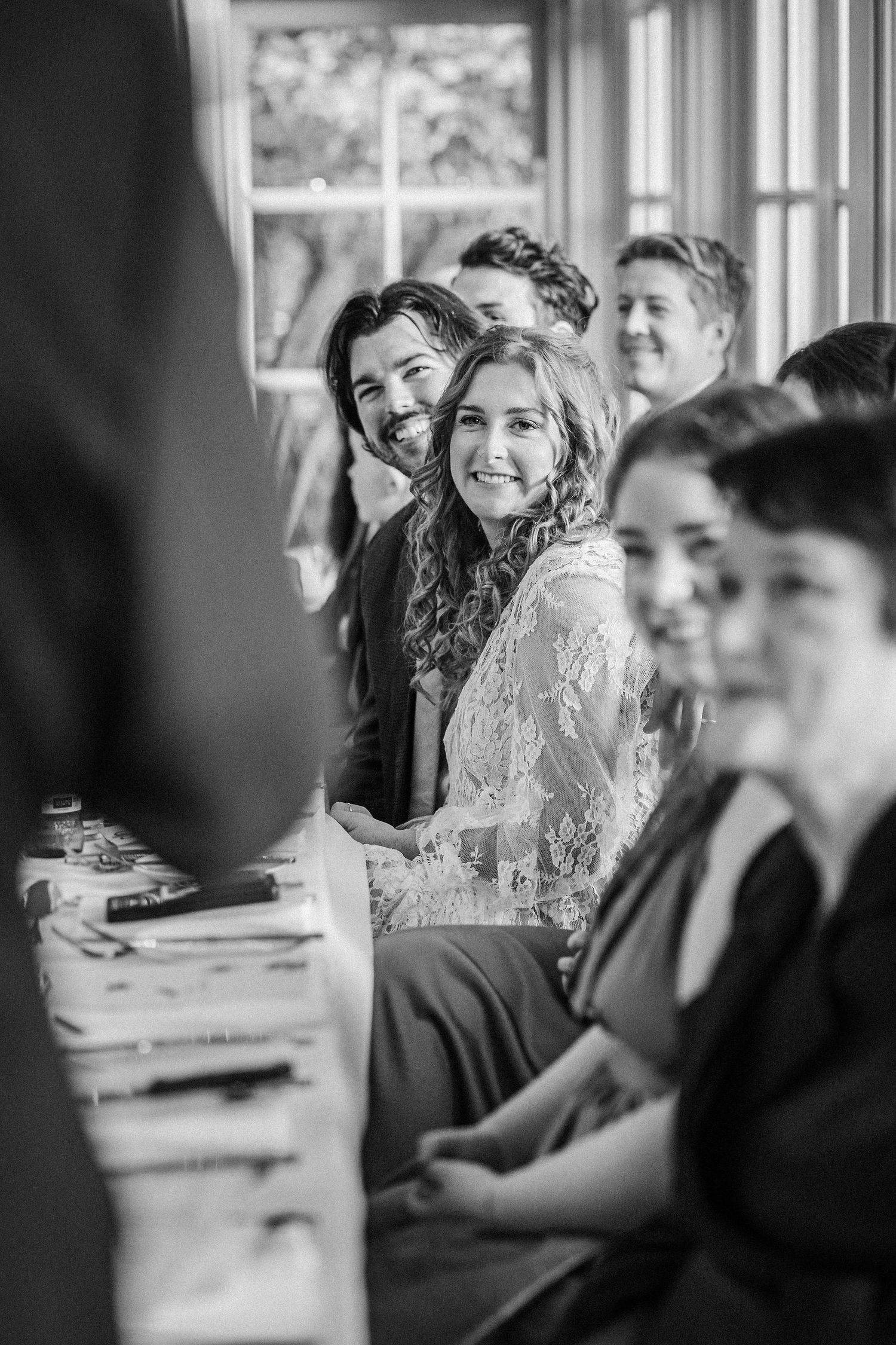Black and white candid photo of wedding guests laughing and socializing during a reception.