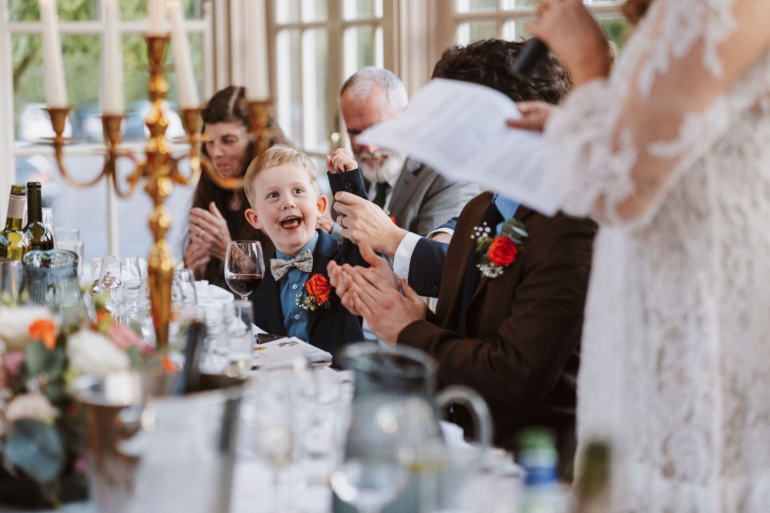 Wedding guests laugh and celebrate during a reception dinner with candelabras and table settings visible.