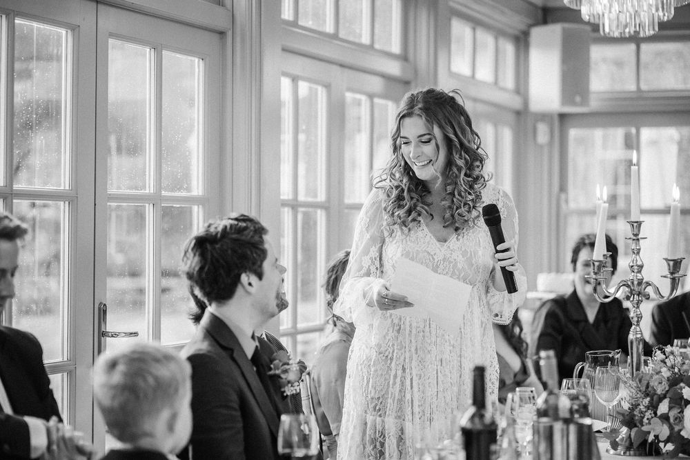 Wedding guests raise their glasses in celebration during an elegant reception in a bright, window-filled venue.