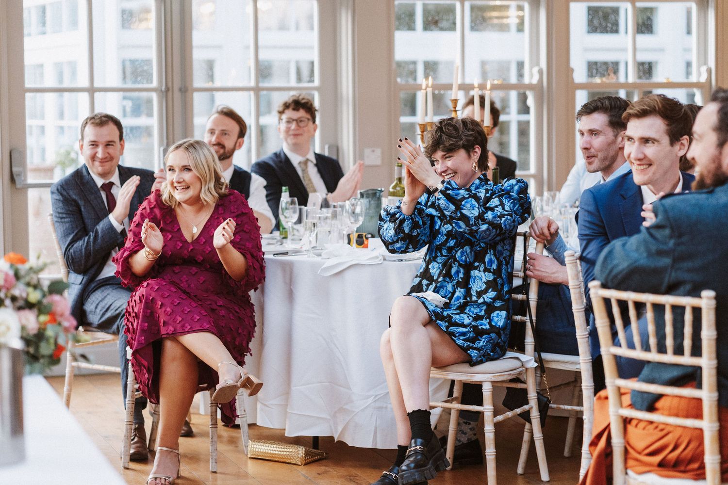 Wedding guests seated in rows of chairs laugh and smile during a joyful ceremony moment.