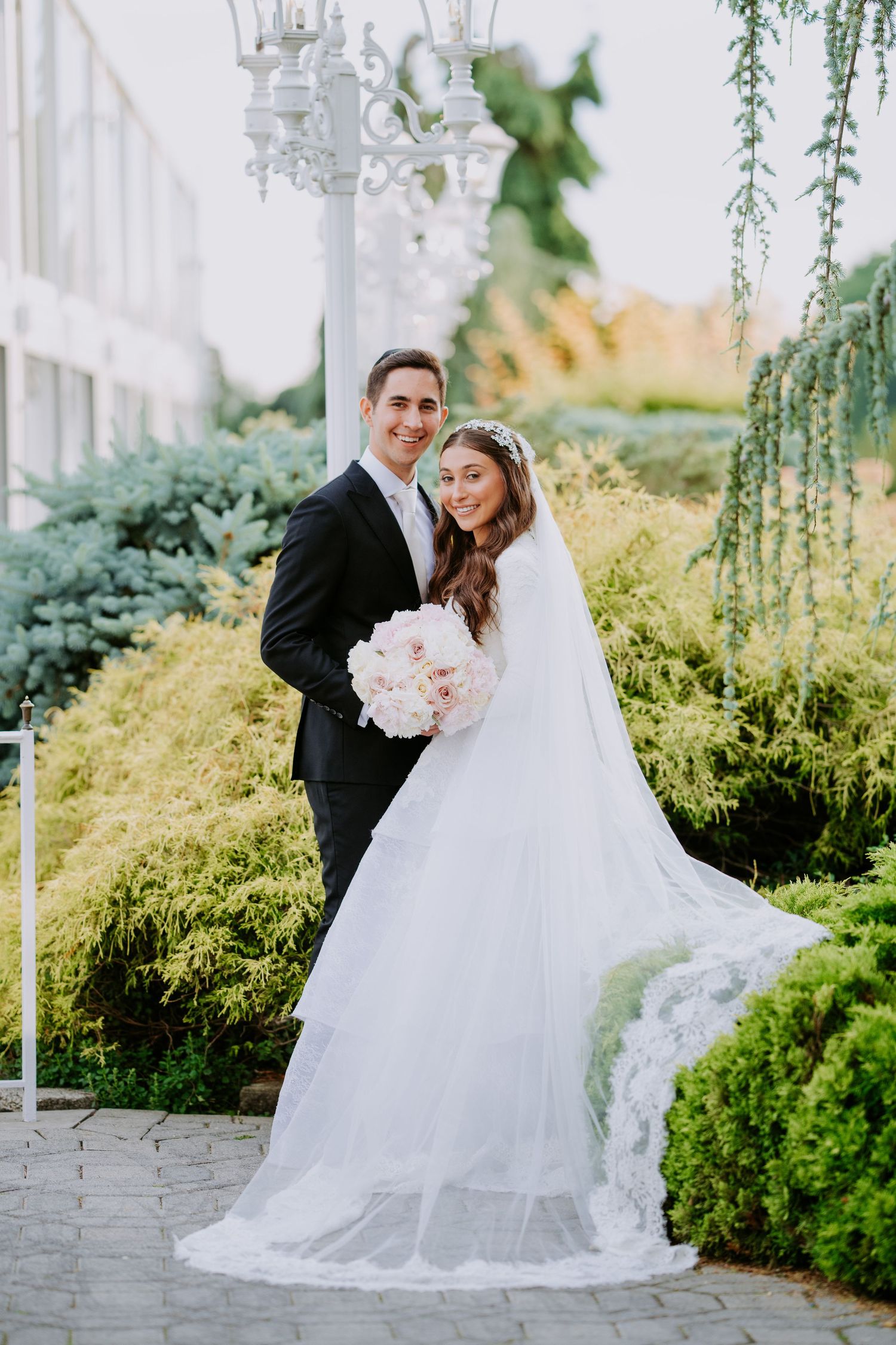 Elegant wedding couple embraces in a grand white hallway with dramatic architectural lighting and geometric patterns.