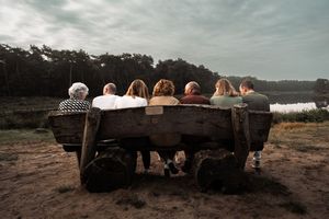 Silhouettes of people sitting on a bench against a moody sunset sky with rolling hills in the background.