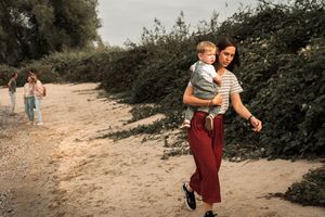 A couple walks along a dusty path through green foliage during a romantic outdoor photoshoot.